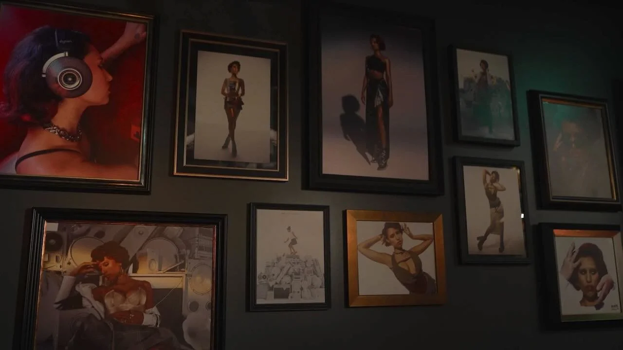Gallery wall with framed photographs of women, including a woman with headphones, a woman in a black dress, and a woman in a white dress, among other fashion images.