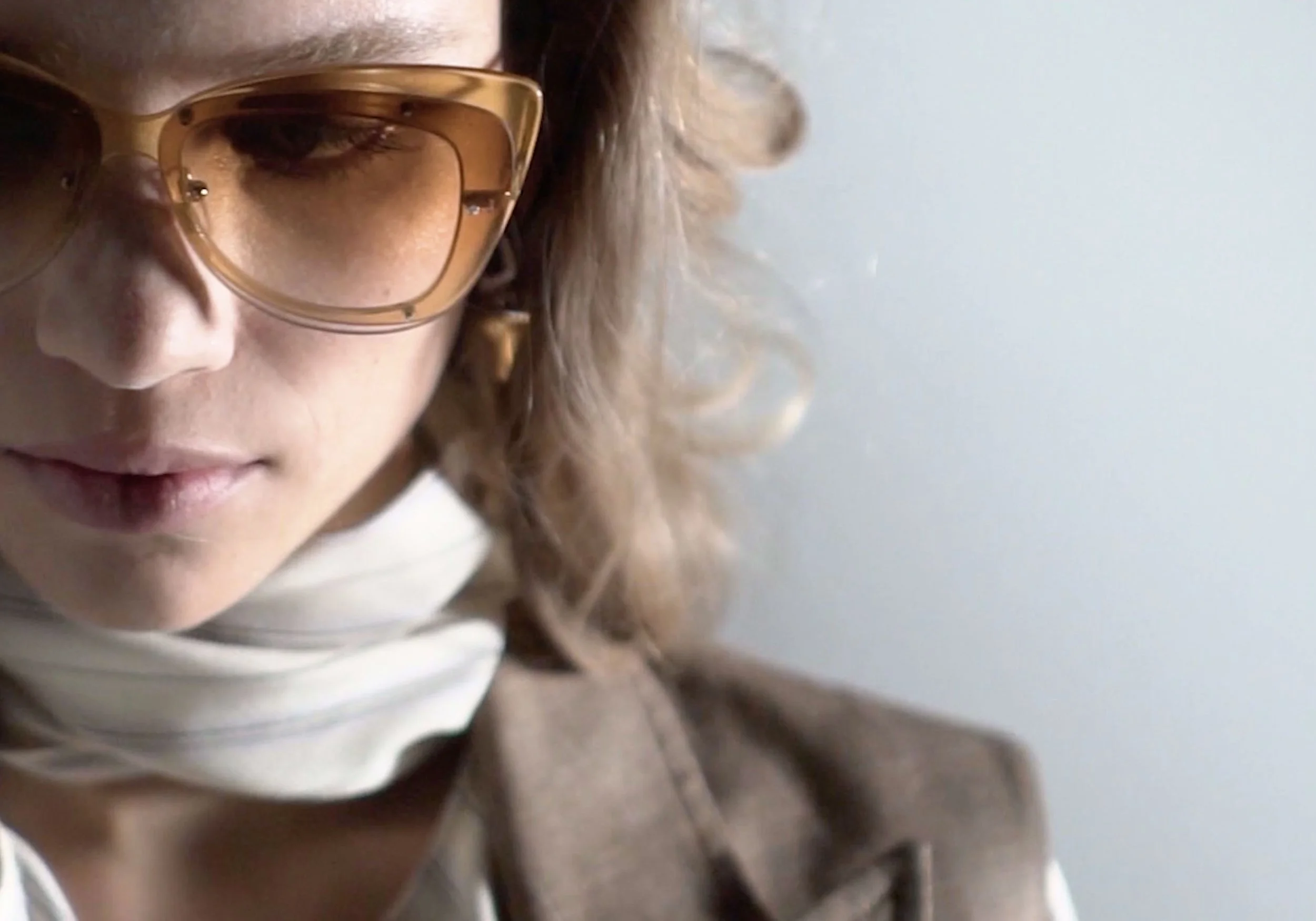 Close-up of a woman with curly hair wearing large brown sunglasses, looking downward, with a neutral expression.