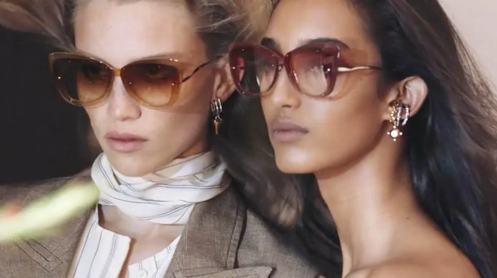 Two women with sunglasses and earrings, glamorous posing closely together.