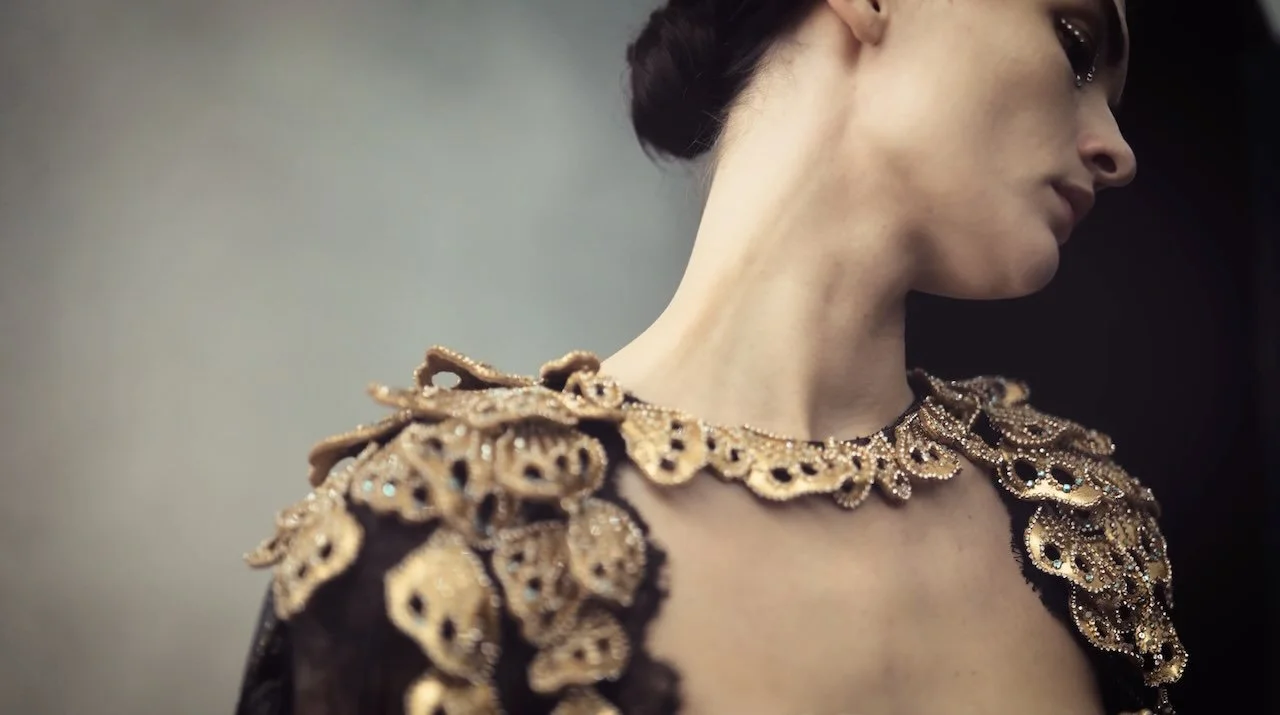 A woman wearing a glamorous black dress with gold embellishments on the shoulders and neckline, showcasing a vintage style.