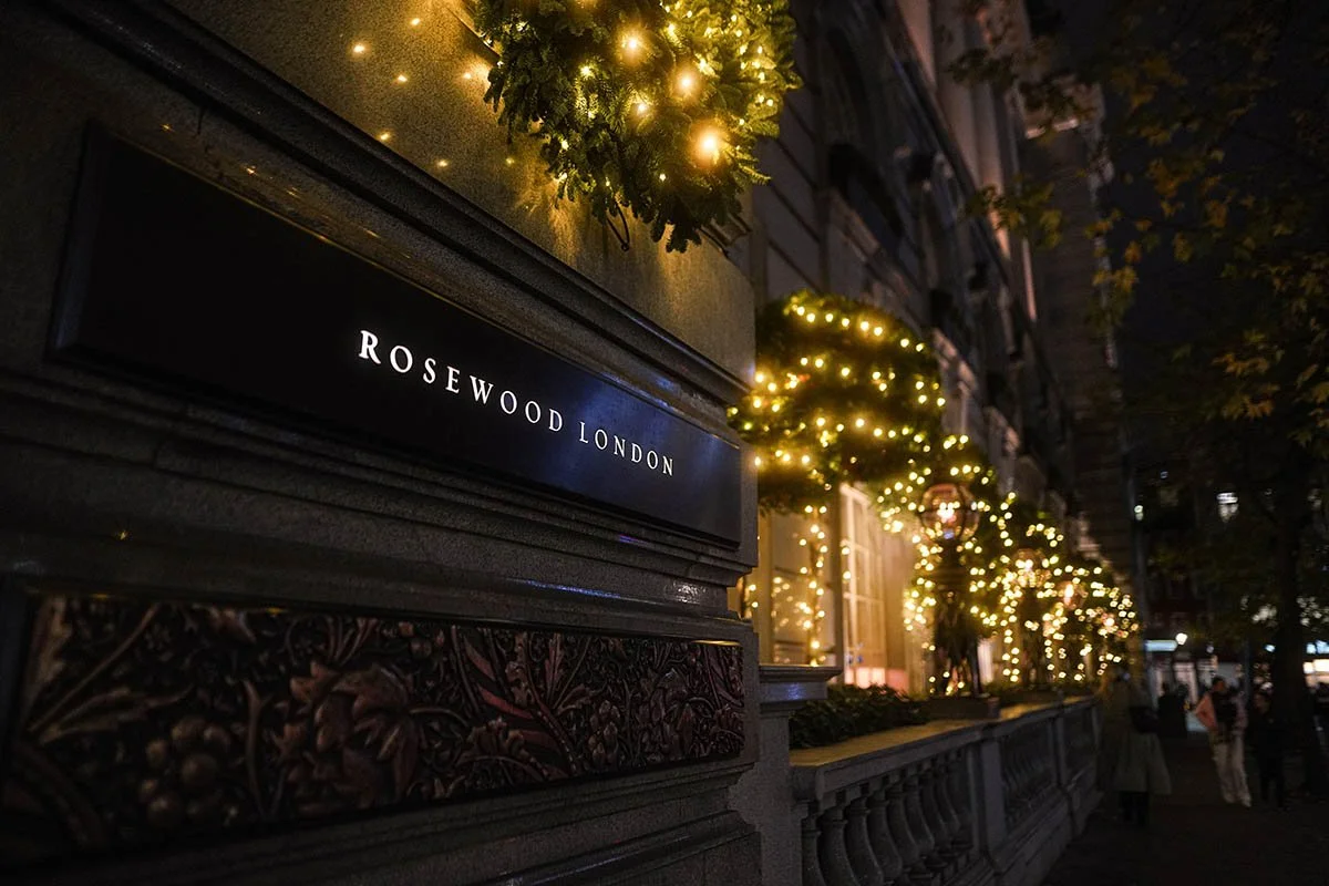 Nighttime street scene outside Rosewood London hotel decorated with Christmas lights and greenery.