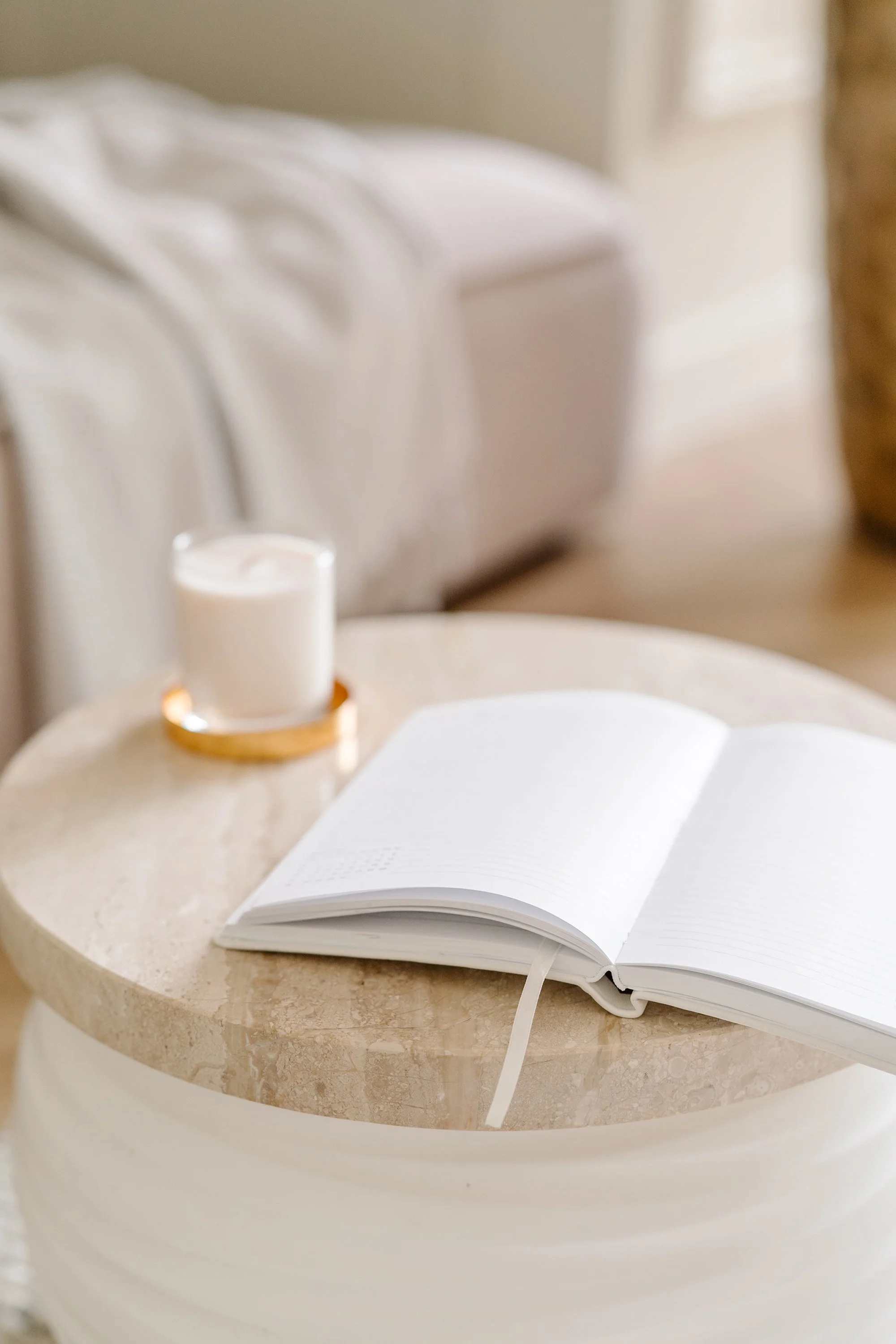 Open blank notebook with a ribbon bookmark, on a light beige marble table, in a cozy room with sunlight.