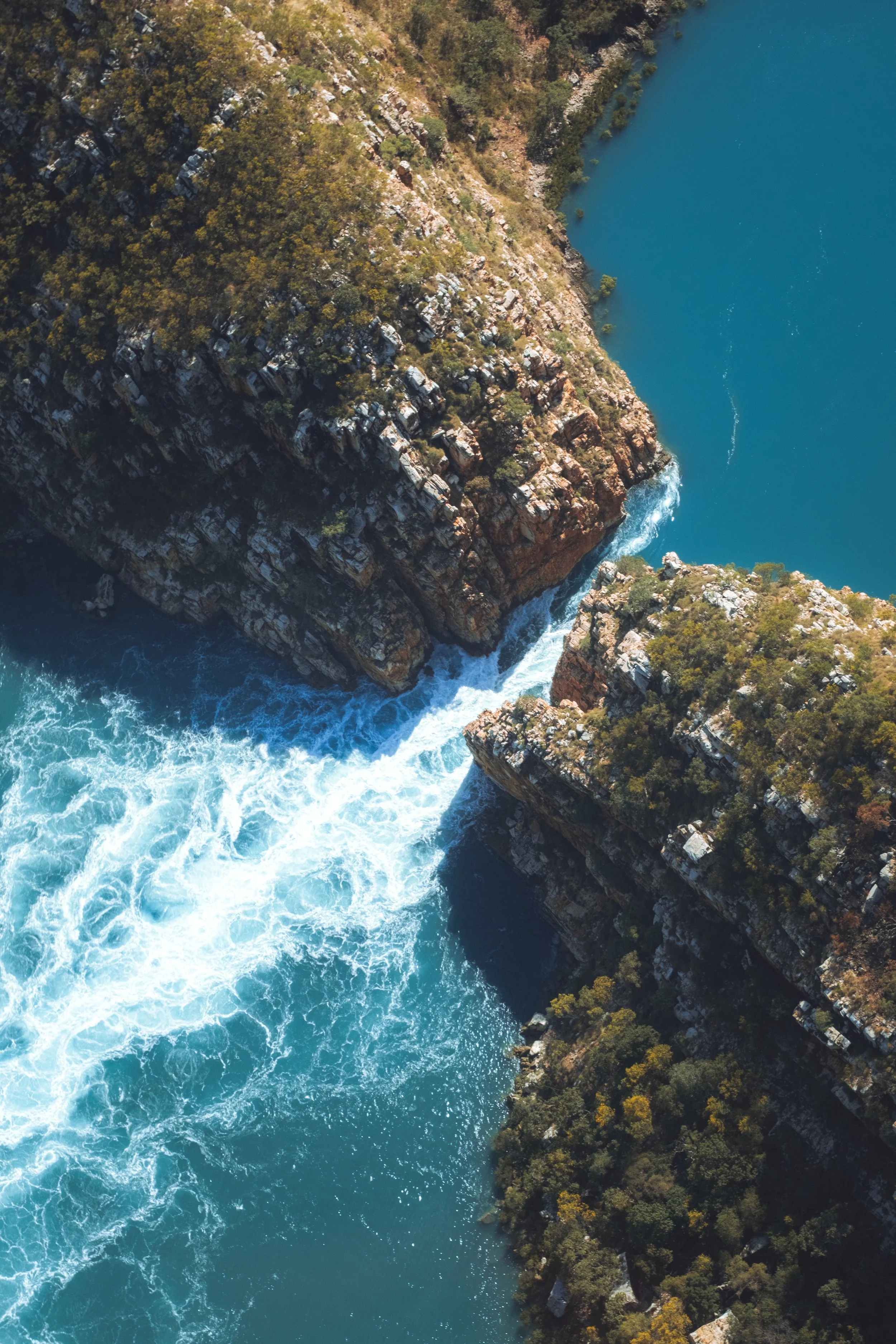 Vues aériennes de falaises rocheuses surplombant une rivière à l'eau bleue, entourée de végétation. Australie