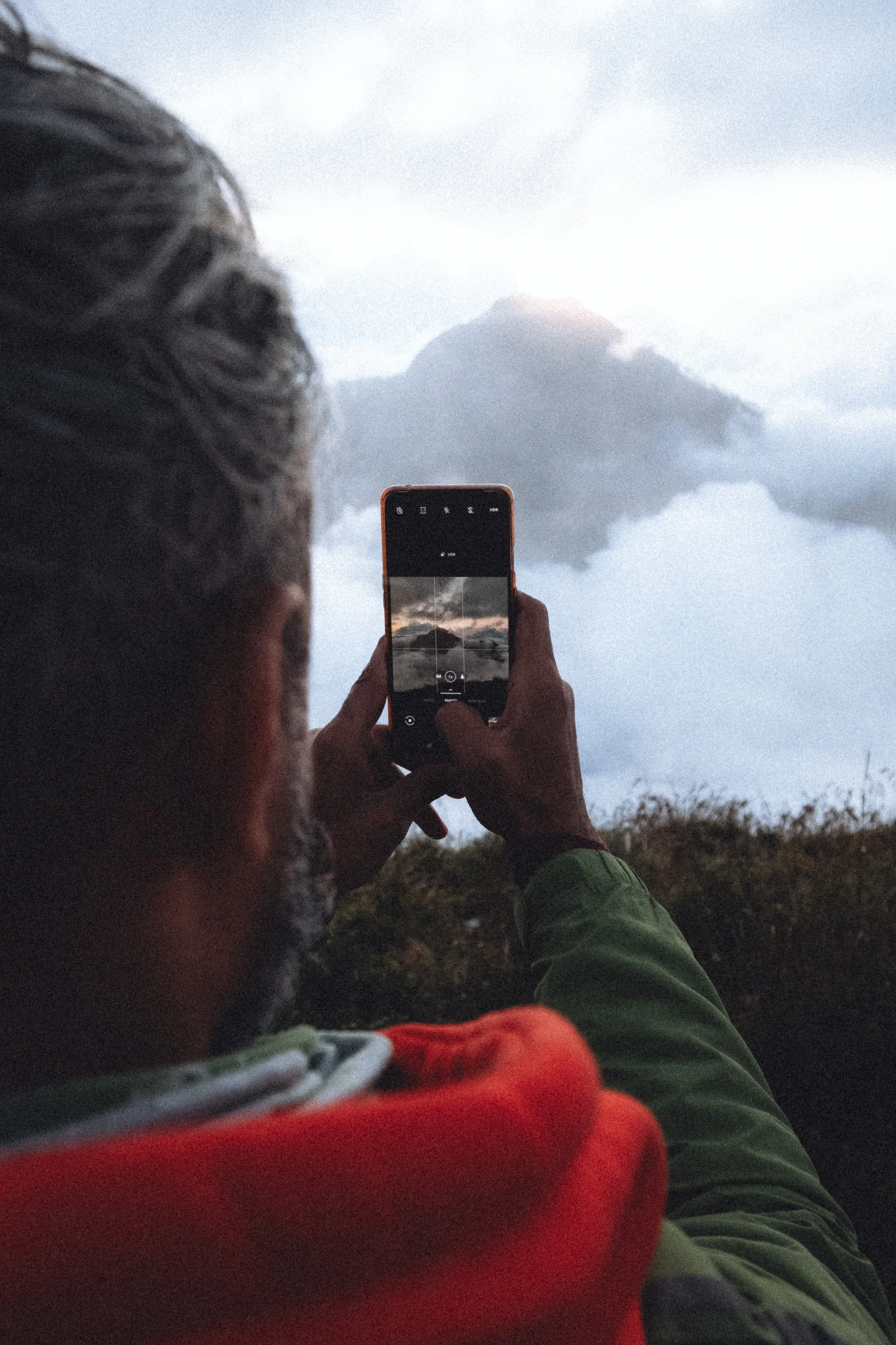Une personne photographiant une montagne dans un paysage nuageux avec un smartphone.Mont Rinjani