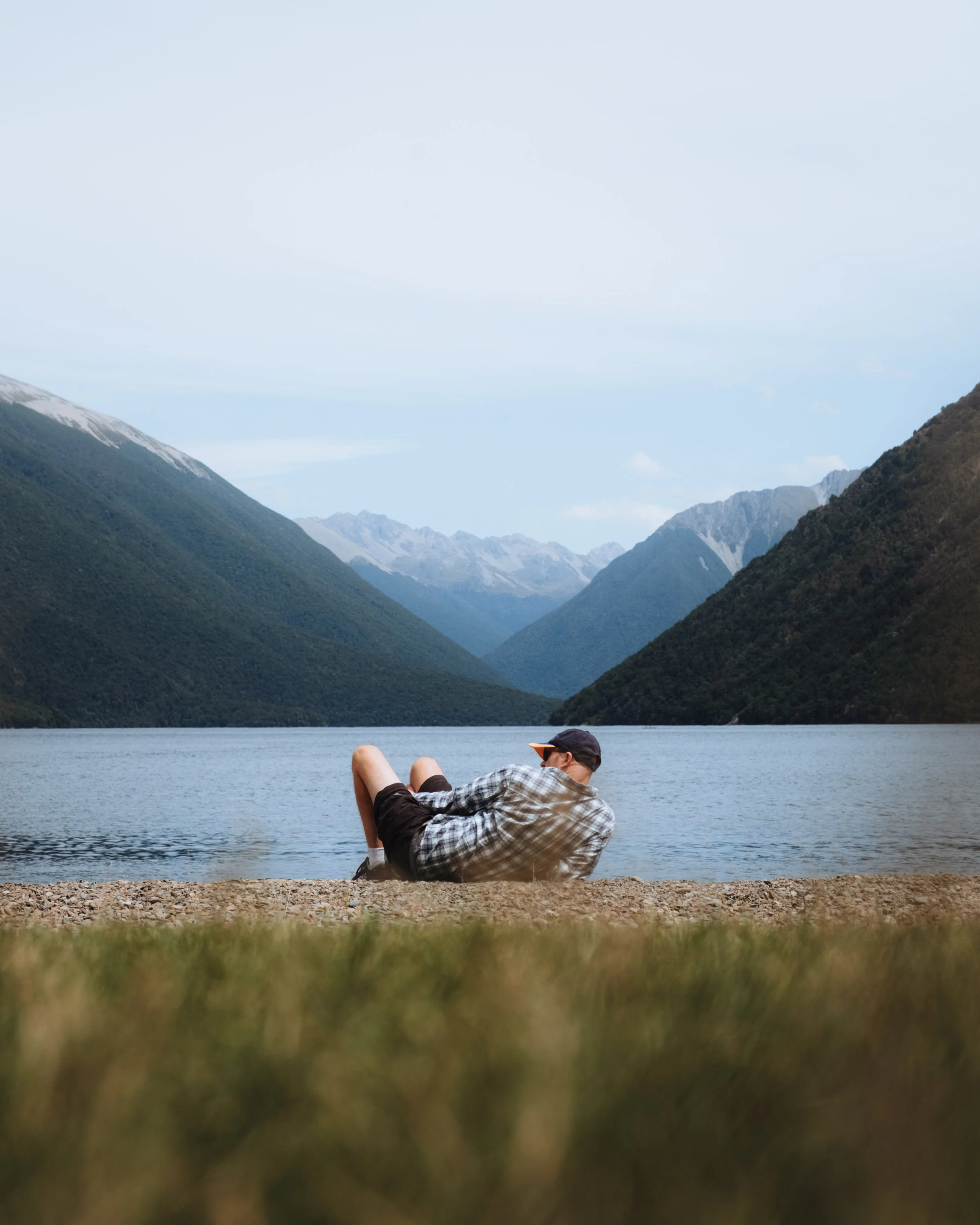 Un homme allongé sur la berge d'un lac entouré de montagnes verdoyantes.