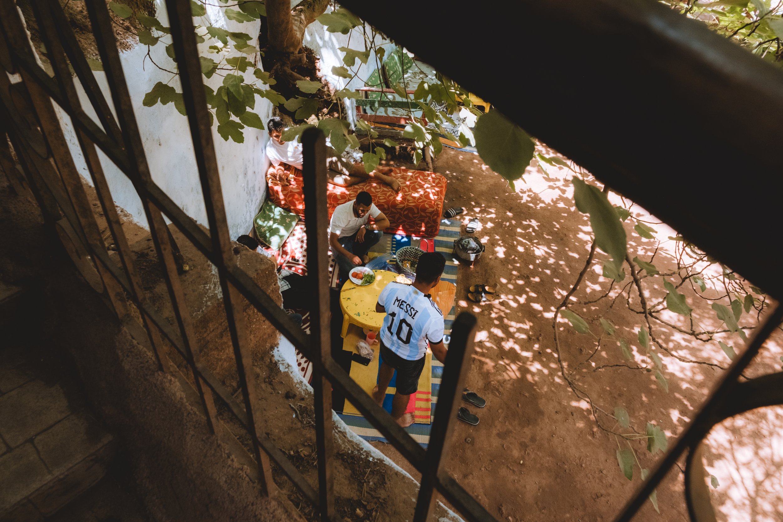 Groupe de personnes ayant un repas, vu d'en haut à travers une clôture en fer, avec un jeune homme portant un maillot de football Messi 10.