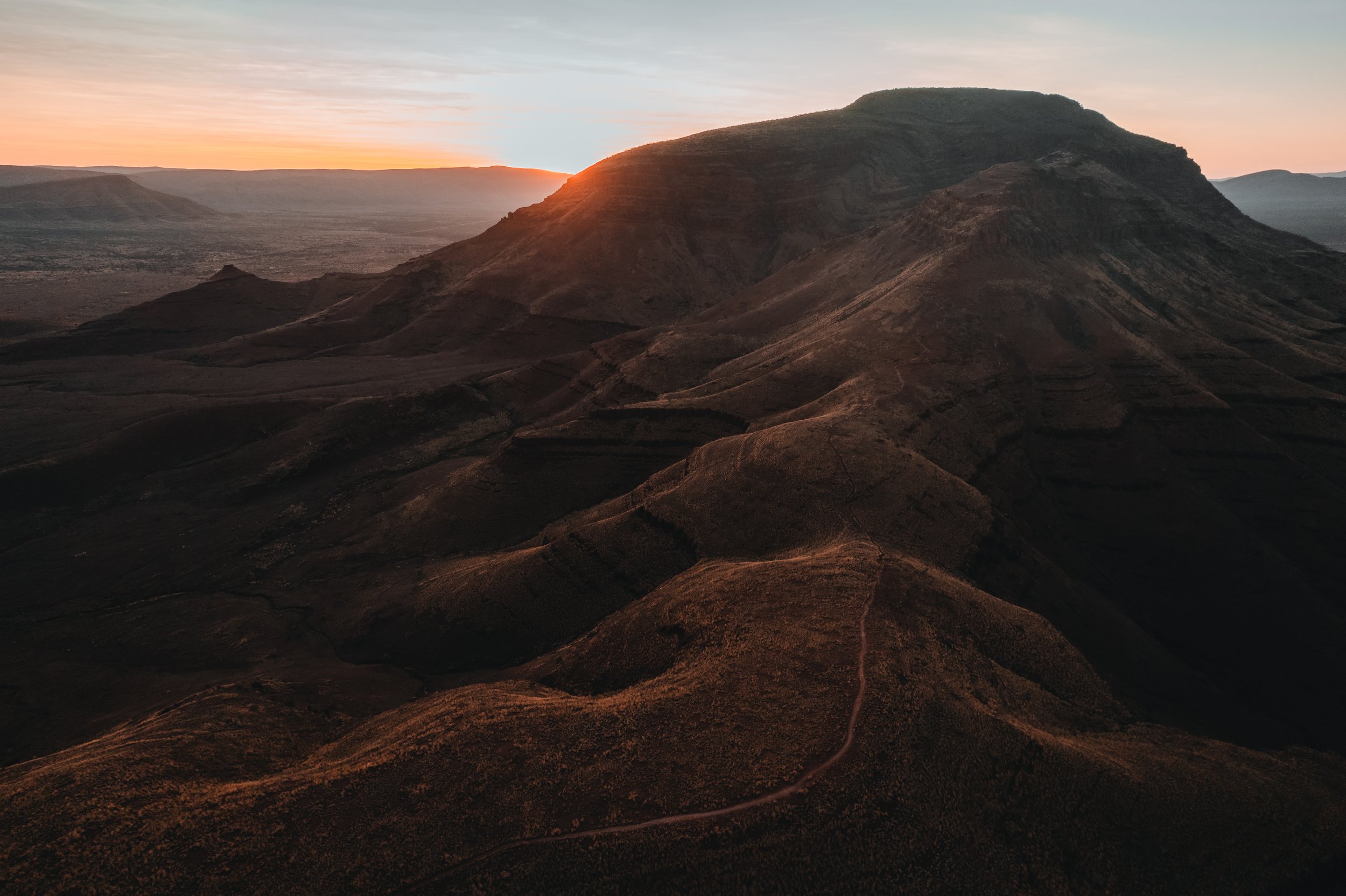 Couchers de soleil sur un paysage montagneux avec un sentier serpentant à travers la terrain rocheux et désertique.