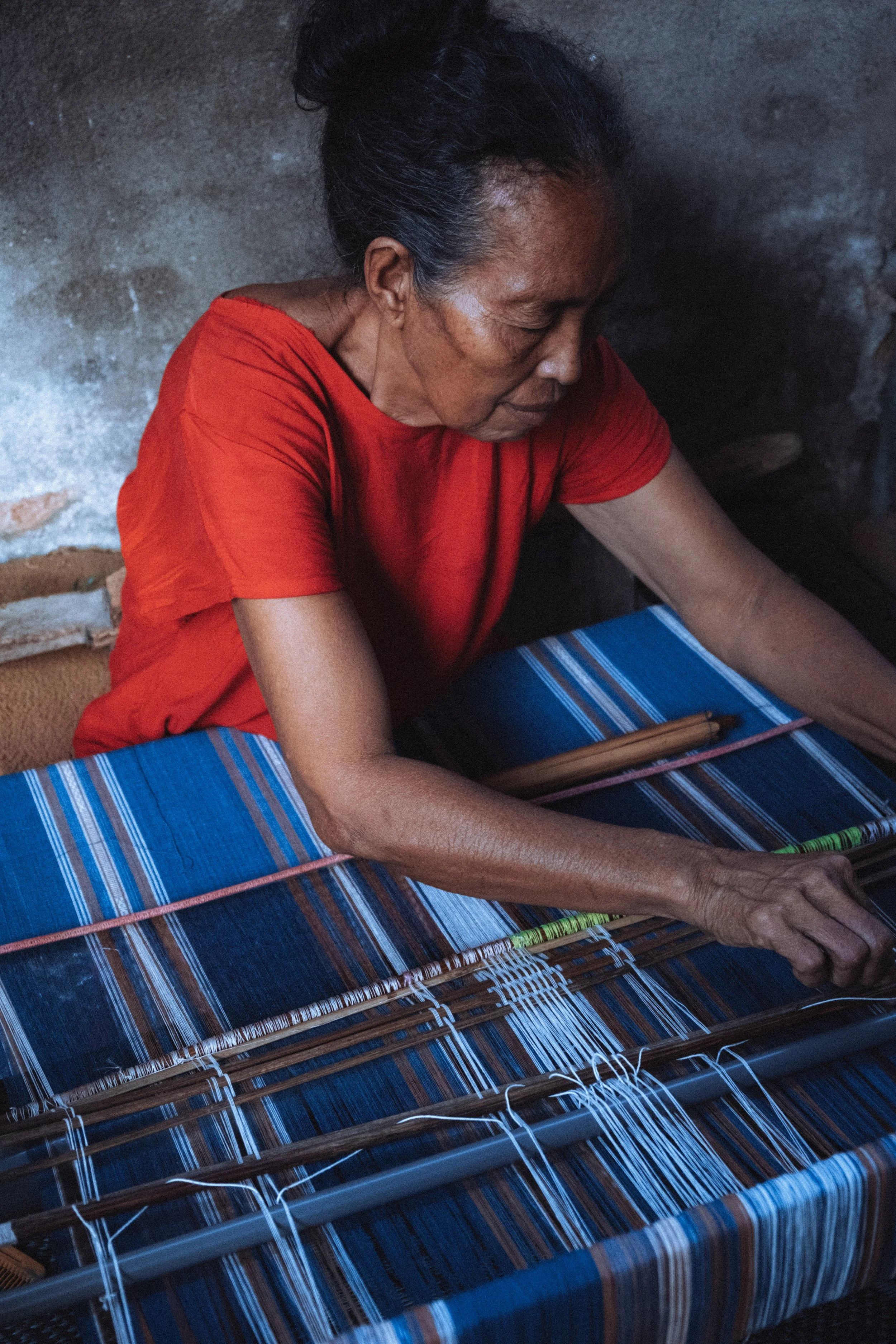 Femme âgée tissant du tissu à la main dans une pièce sombre.