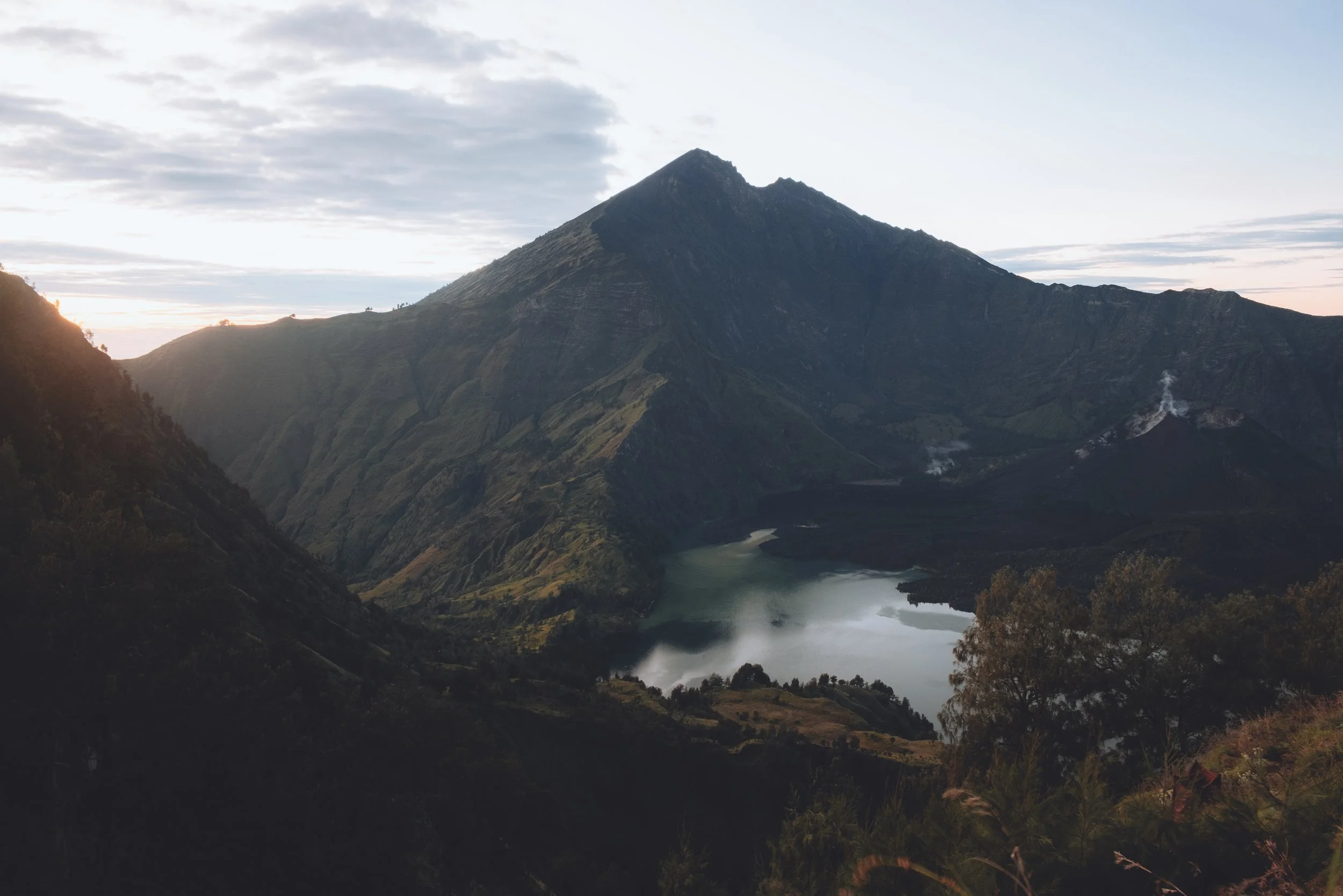 Montagne volcanique avec un lac au fond, sous un ciel partiellement nuageux. Mont Rinjani