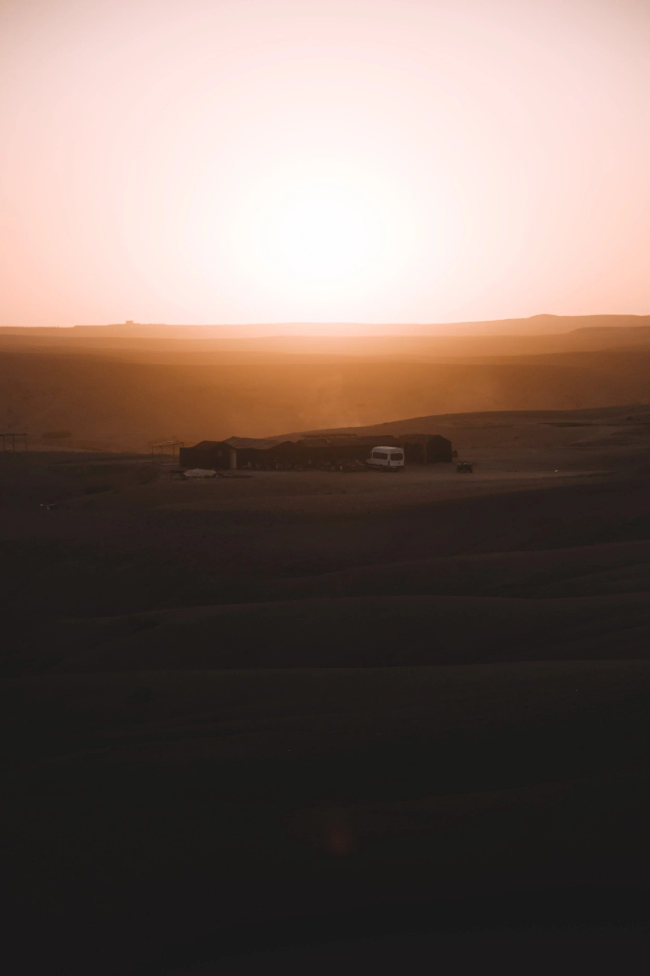 Paysage désertique au coucher du soleil avec des bâtiments et une caravane en premier plan.