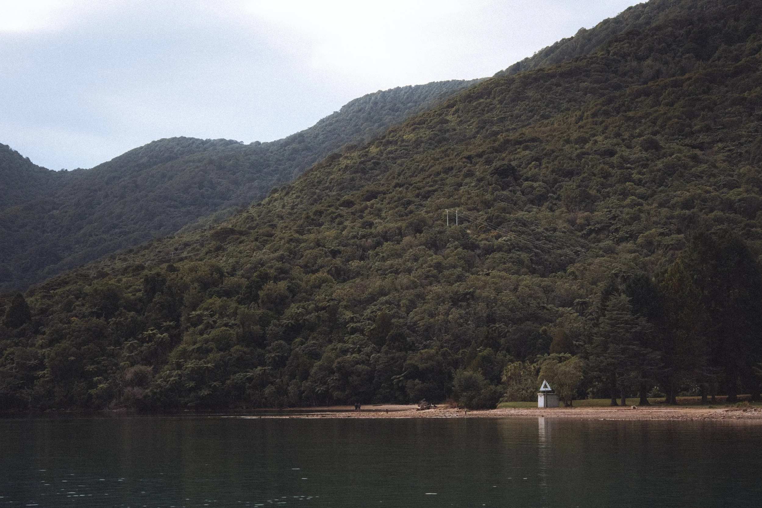 Montagnes vertes près d'un lac calme avec une petite cabane blanche sur la rive.