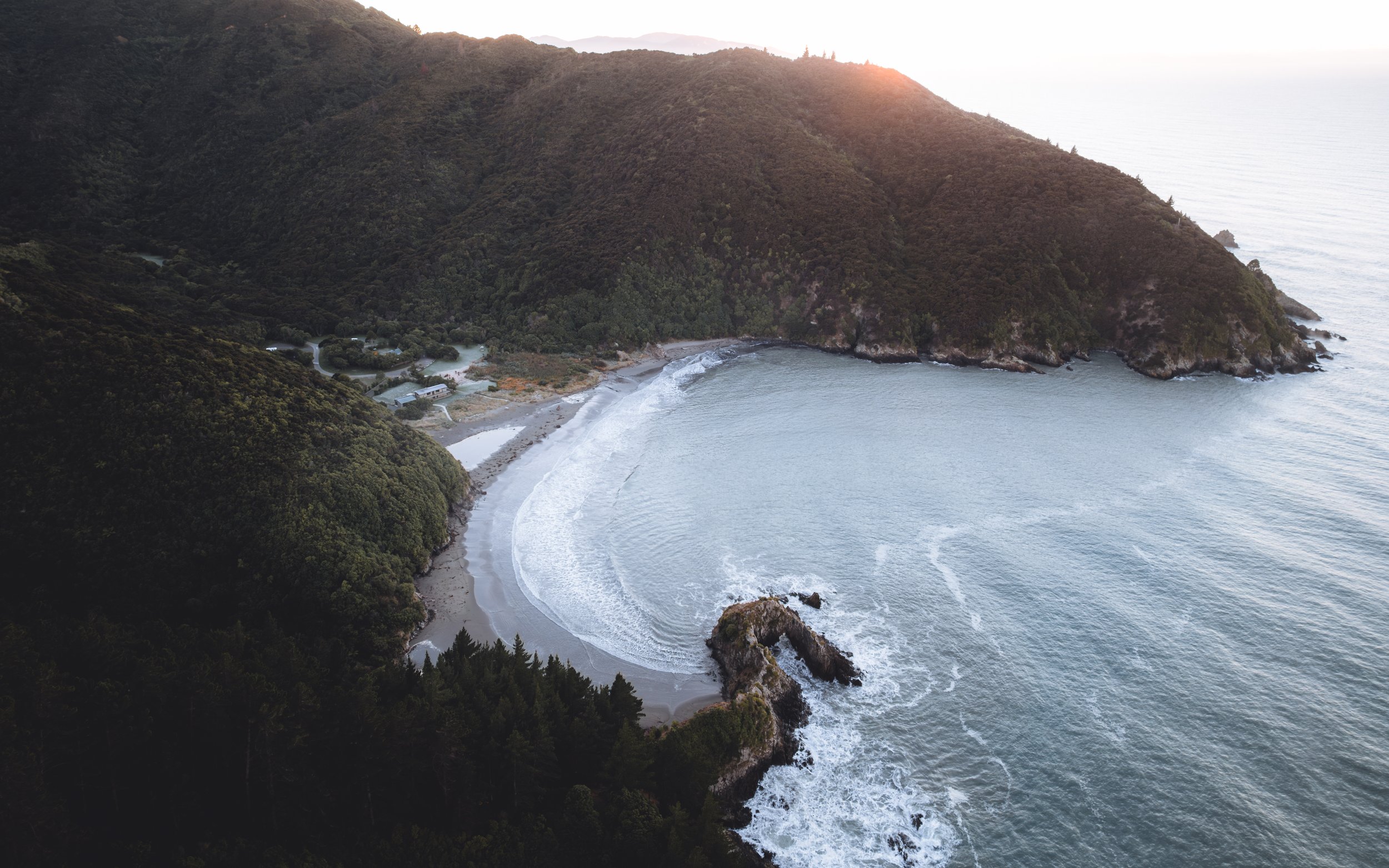 Vue de la côte rocheuse et de la plage entourée de montagnes verdoyantes au coucher du soleil.