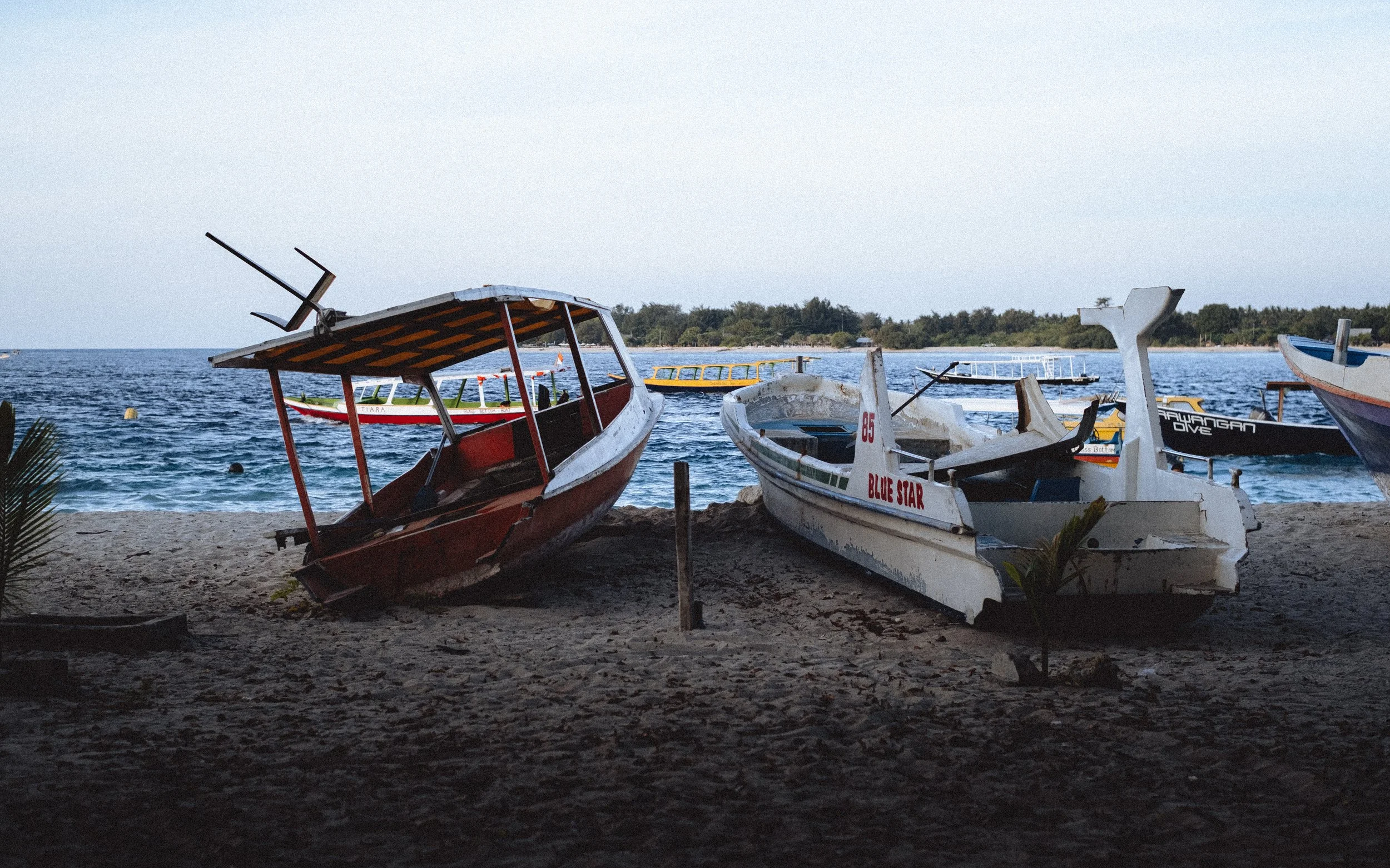 Deux vieux bateaux échoués sur la plage, avec la mer et d'autres bateaux en arrière-plan.