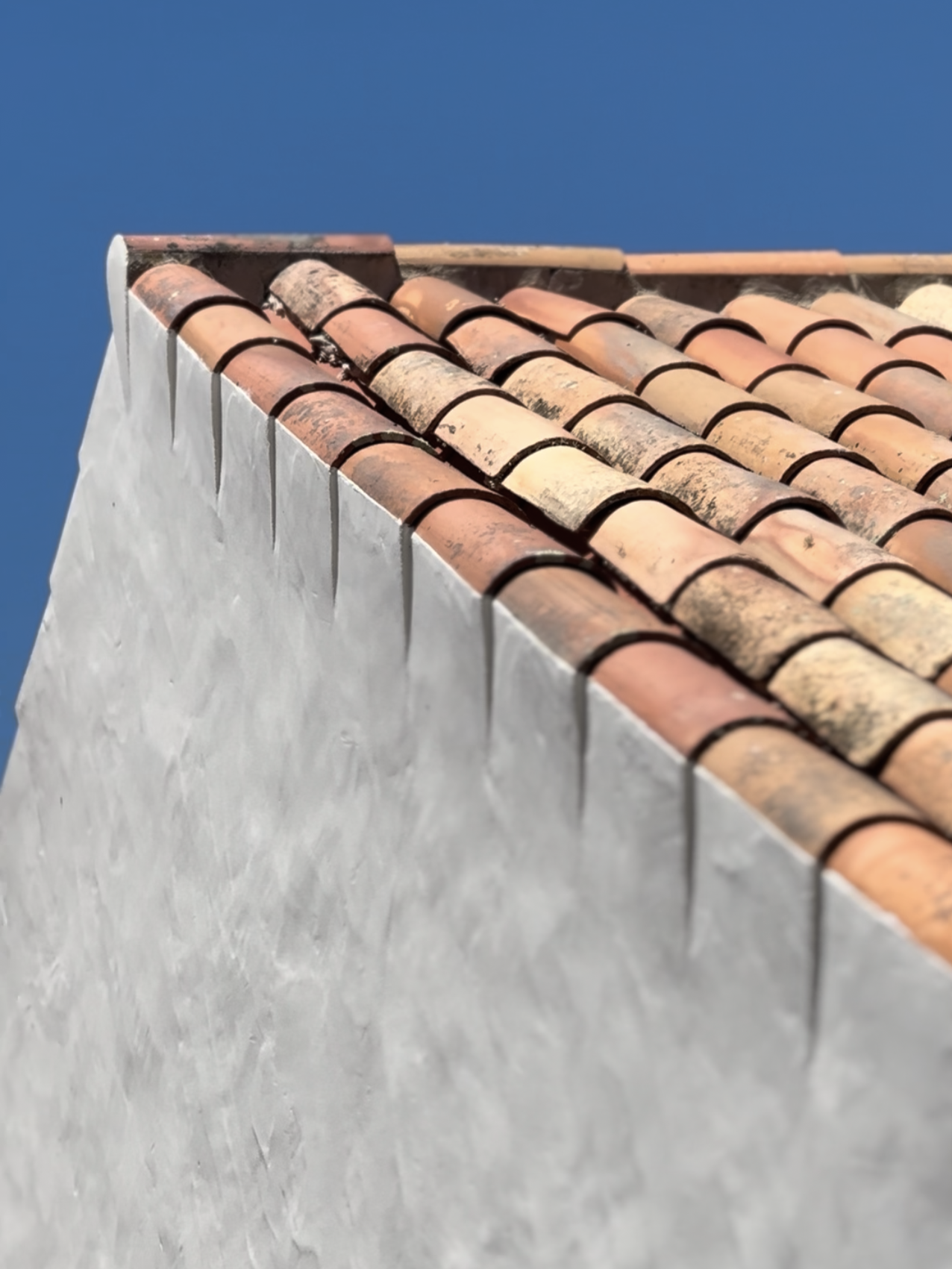 Close-up of roof tiles on a white building against a clear blue sky.