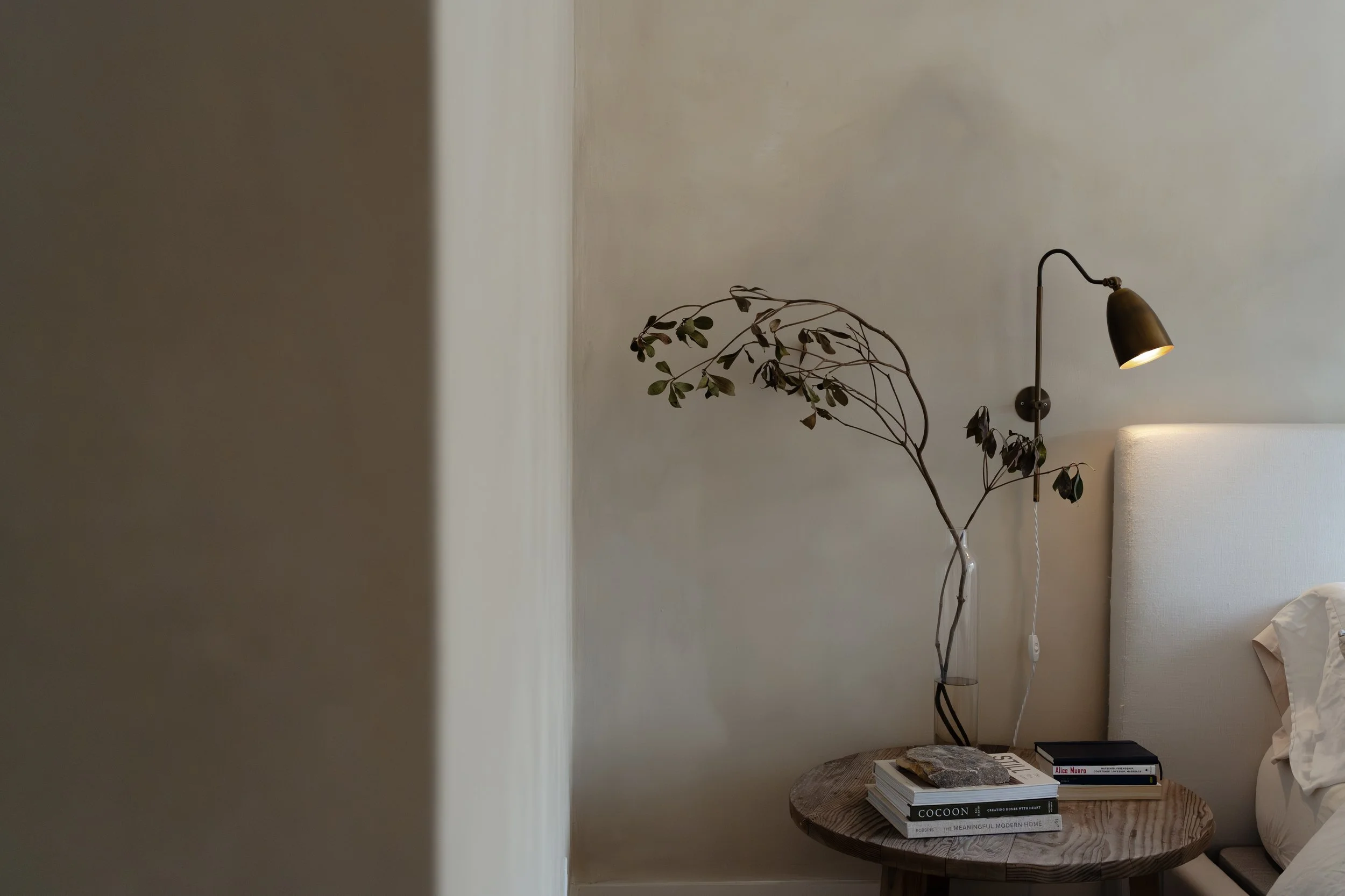 A picture of a bedroom highlighting the textured painted wall with a wood side table and brass lamp hanging beside the bed.
