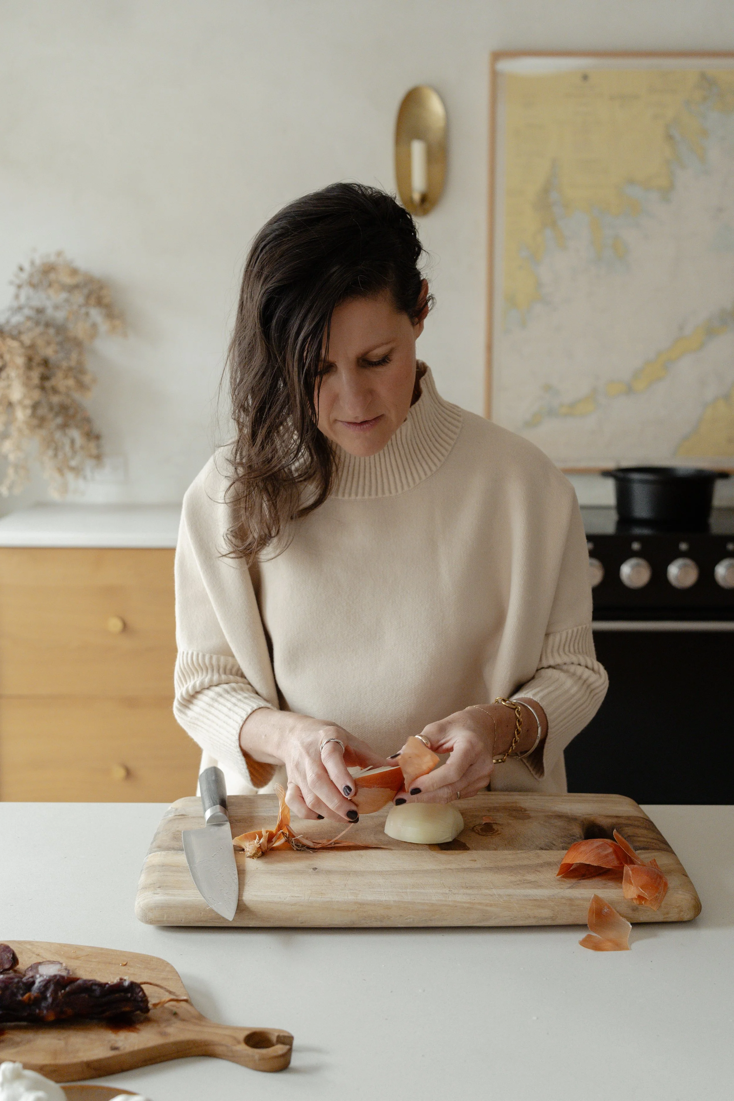 A photo of a woman chopping onions in a kitchen while wearing an ivory sweater.