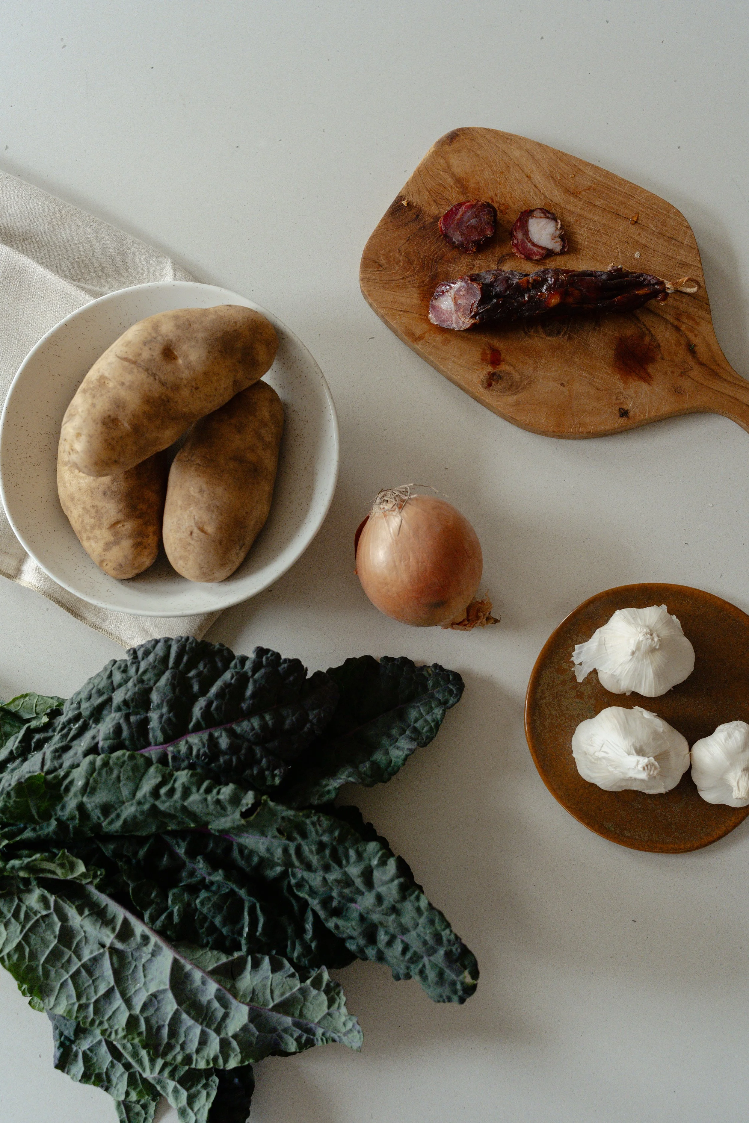 An overhead photo of ingredients on a countertop. The ingredients include potatoes, sausage, garlic and fresh kale.