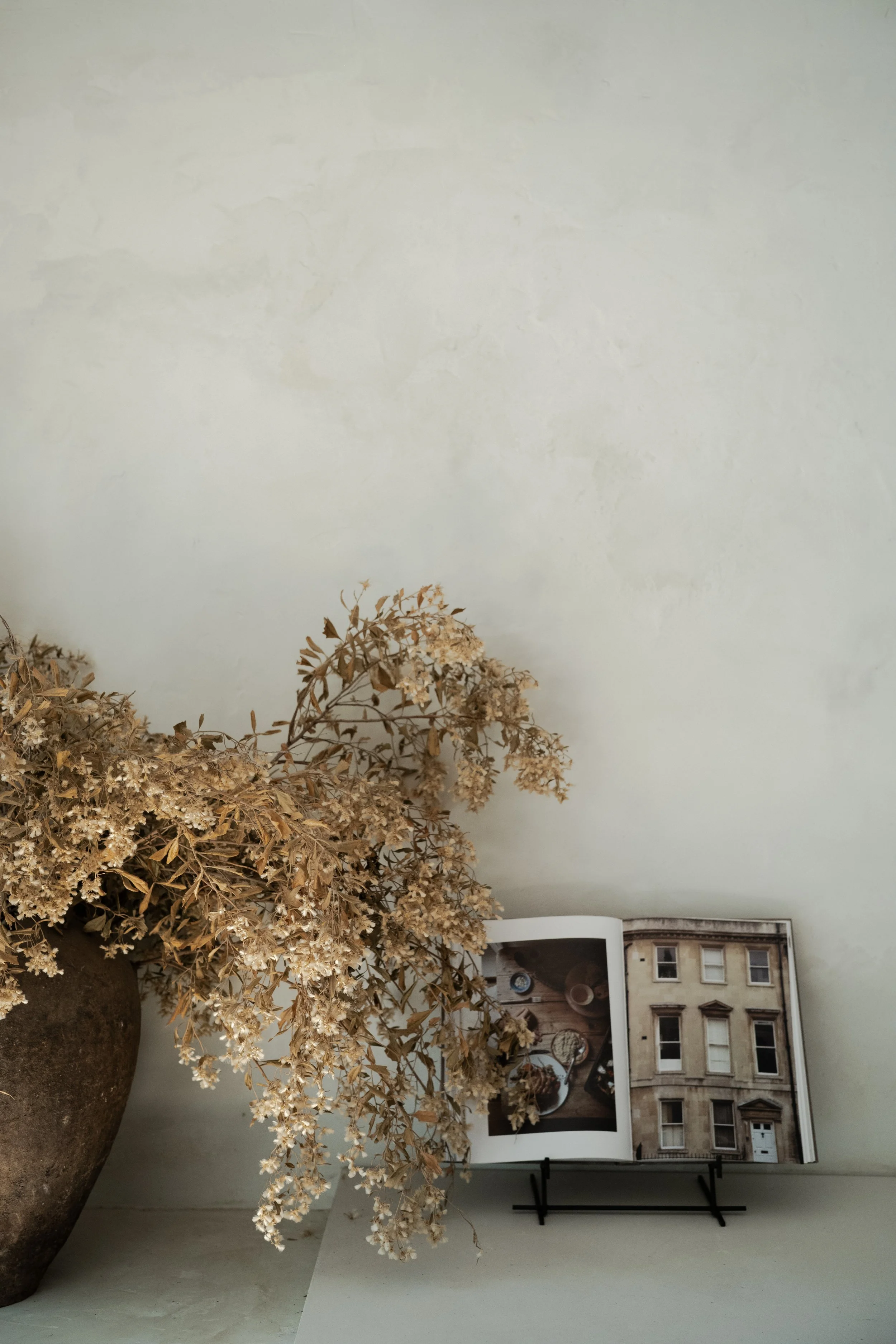 An image of a dried arrangement of flowers on a neutral backdrop with a tabletop kitchen book on display.