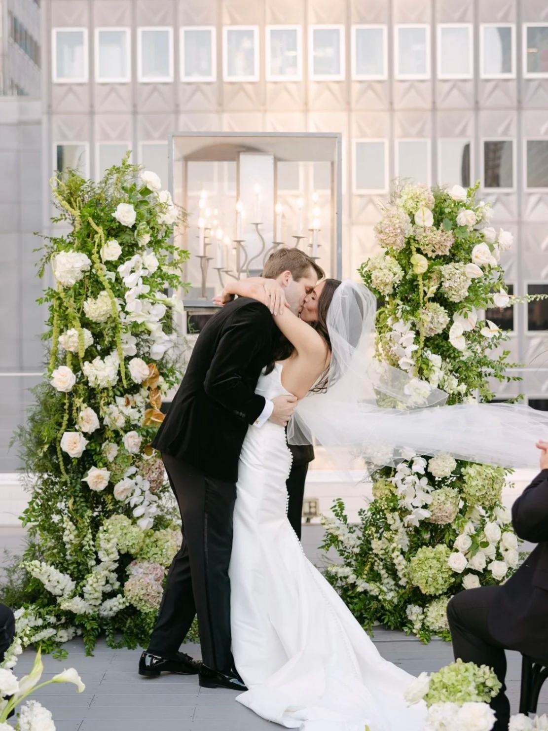 Bride and groom kissing at their wedding ceremony surrounded by floral arrangements.