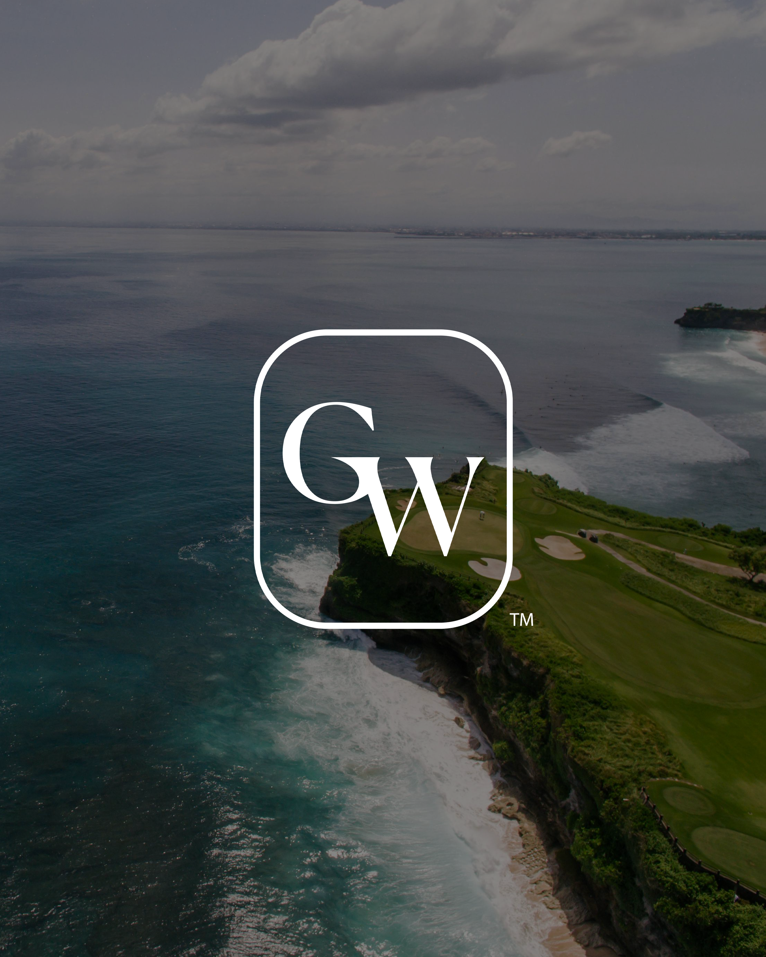 Aerial view of a coastal golf course with ocean waves crashing against the cliffs on a cloudy day.