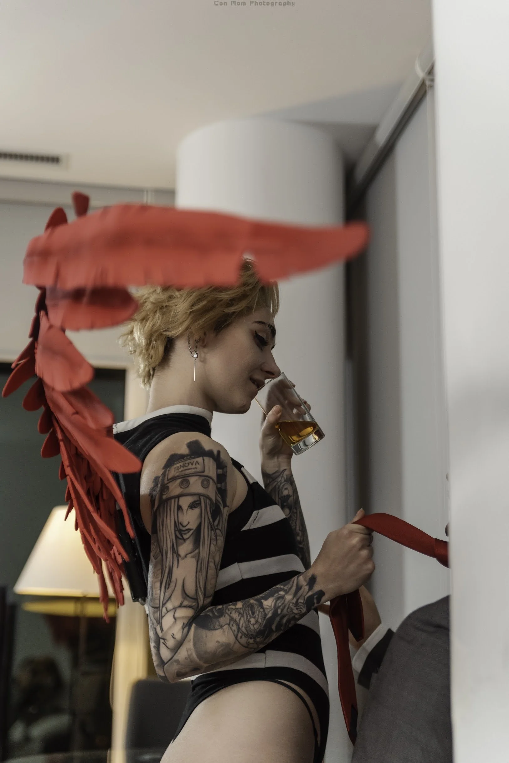 Someone else has entered the condo; Hawks now holds a glass of amber liquid, likely alcohol, and smirks at the newcomer, obscured from view. Hawks is holding the man's red tie.