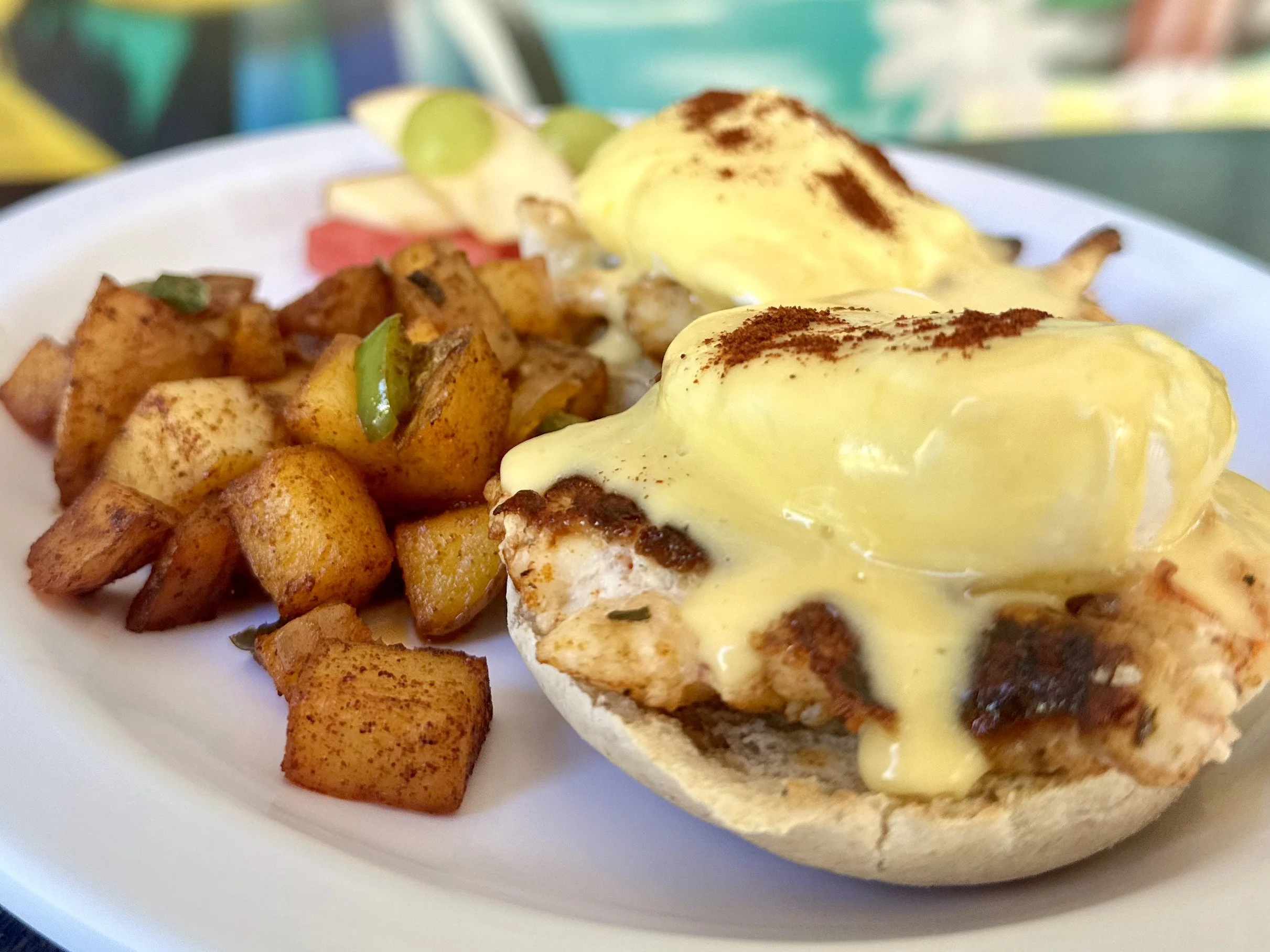 Eggs Benedict with hollandaise sauce, served with breakfast potatoes on a white plate.