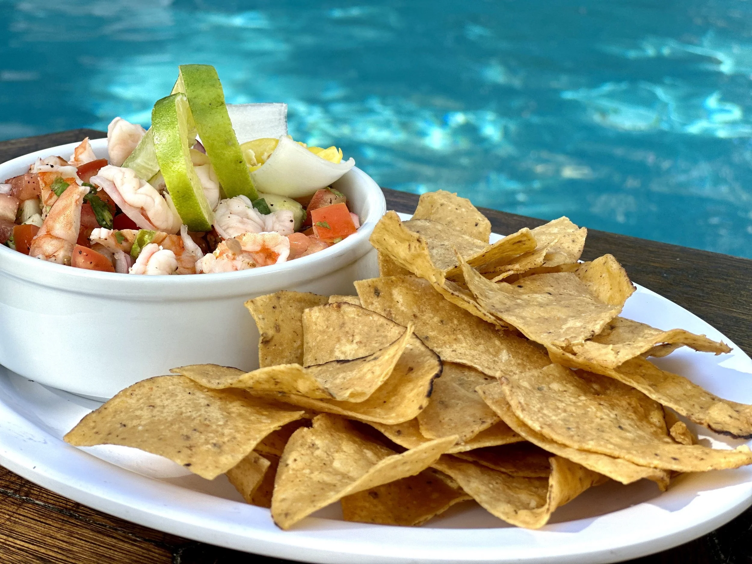 Fresh shrimp ceviche with lime and vegetables served with crispy tortilla chips near a swimming pool.