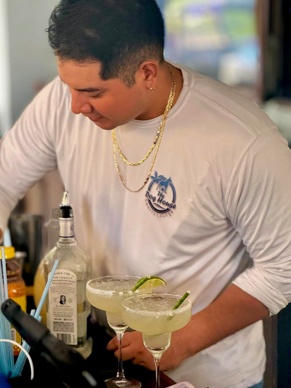 A bartender preparing two margarita cocktails with lime garnishes and salted rims at The Dog House.