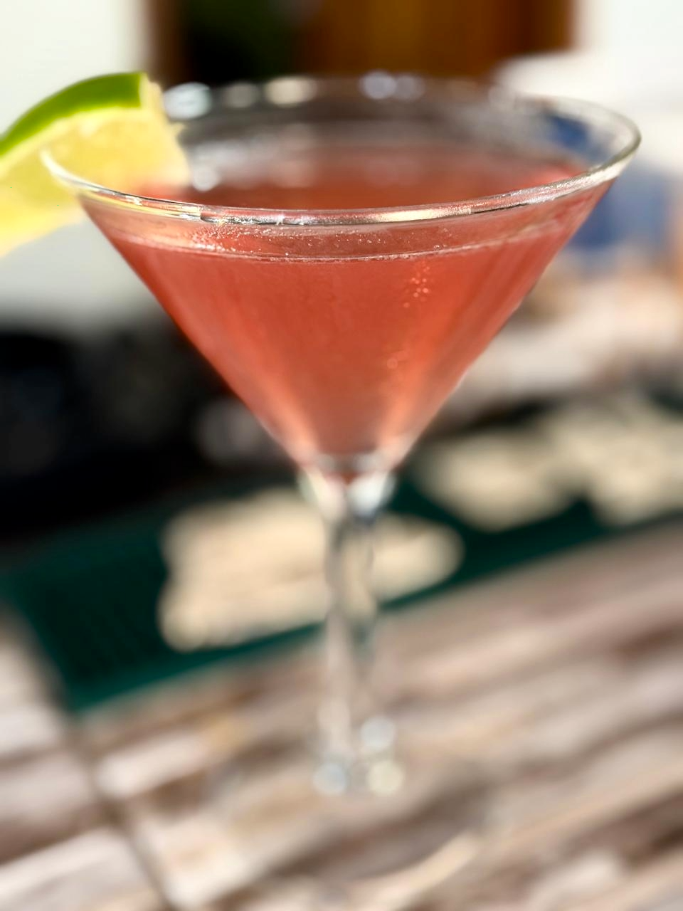 A pink cocktail in a martini glass garnished with a lime wedge.