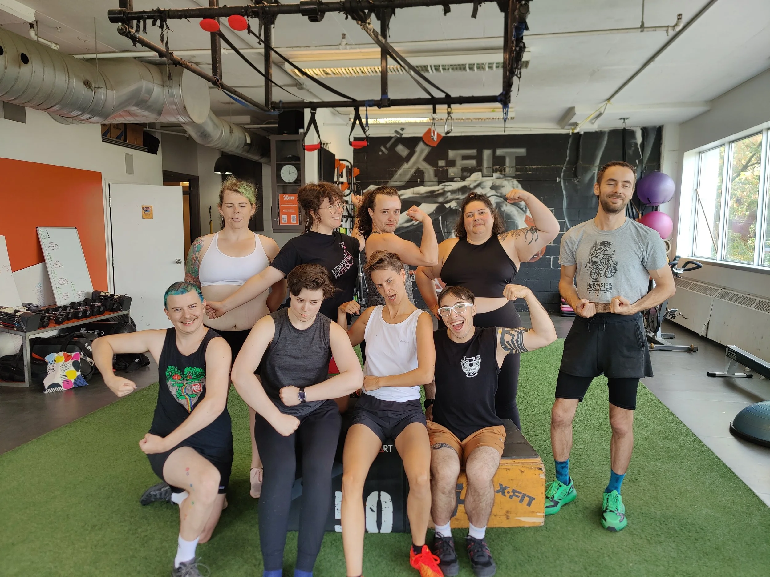 A group of people in a gym pose confidently while flexing their muscles.