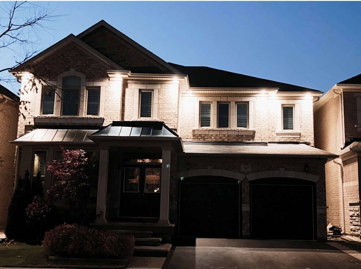 Two-story brick house with exterior lights illuminating the facade and a two-car garage at dusk.