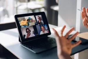 A person participating in a virtual meeting on a laptop, with their hands gesturing near the device.