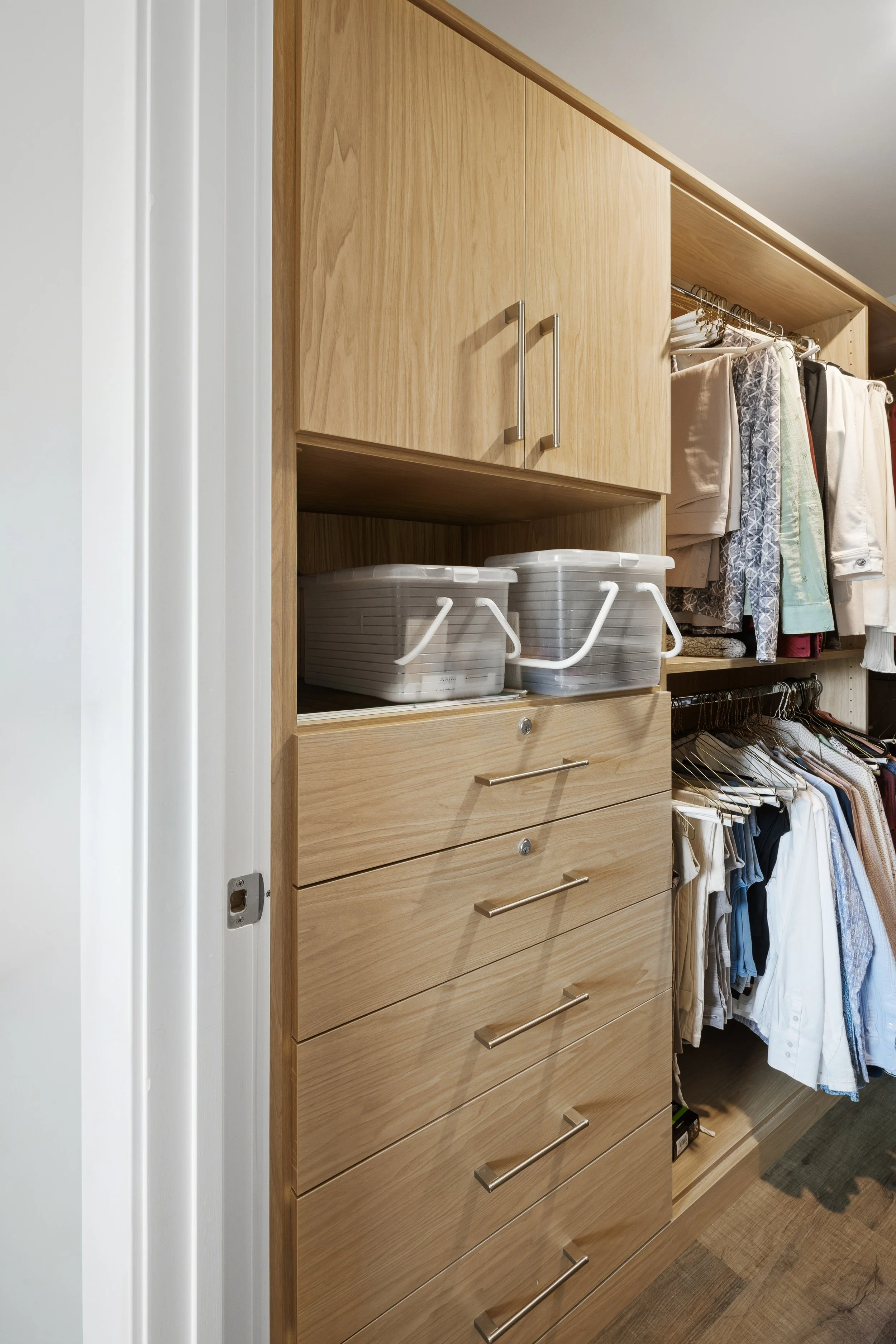 Closet with wooden drawers and shelves, clothes hanging on rods, plastic storage boxes on open shelf