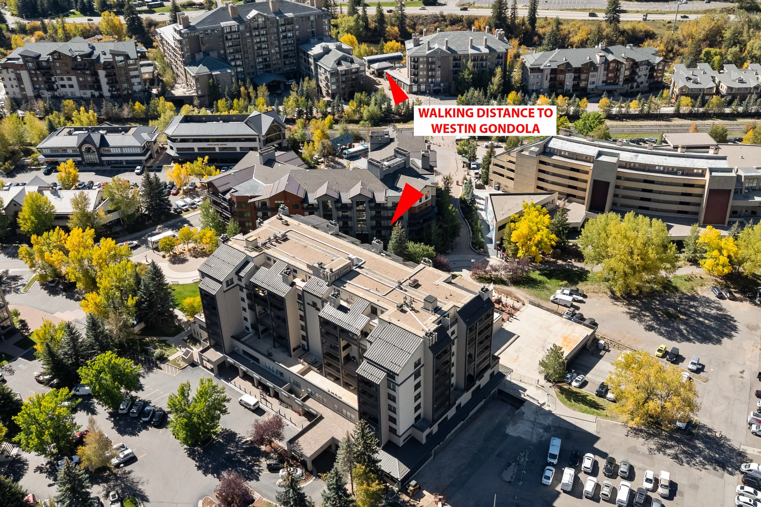 An aerial view of a cityscape with multiple high-rise apartments and parking lots surrounded by green trees. Two red arrows with text indicate walking distance to a westin gondola. The area appears to be part of a developed urban neighborhood.