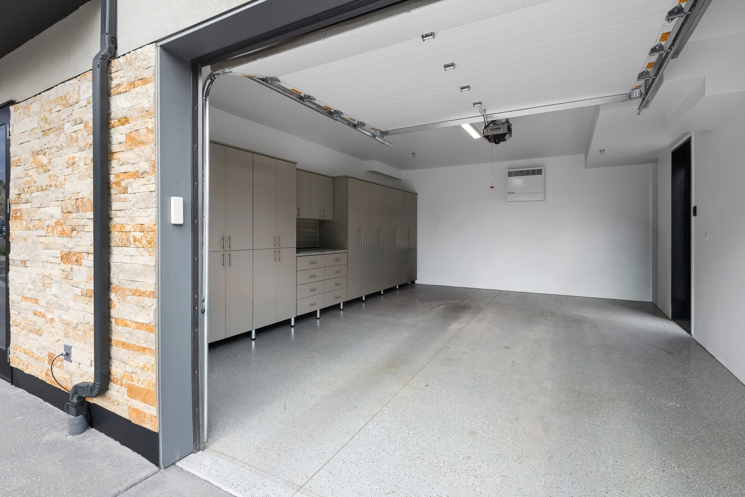 Open garage door revealing a clean modern garage interior with grey cabinets and a speckled grey floor.