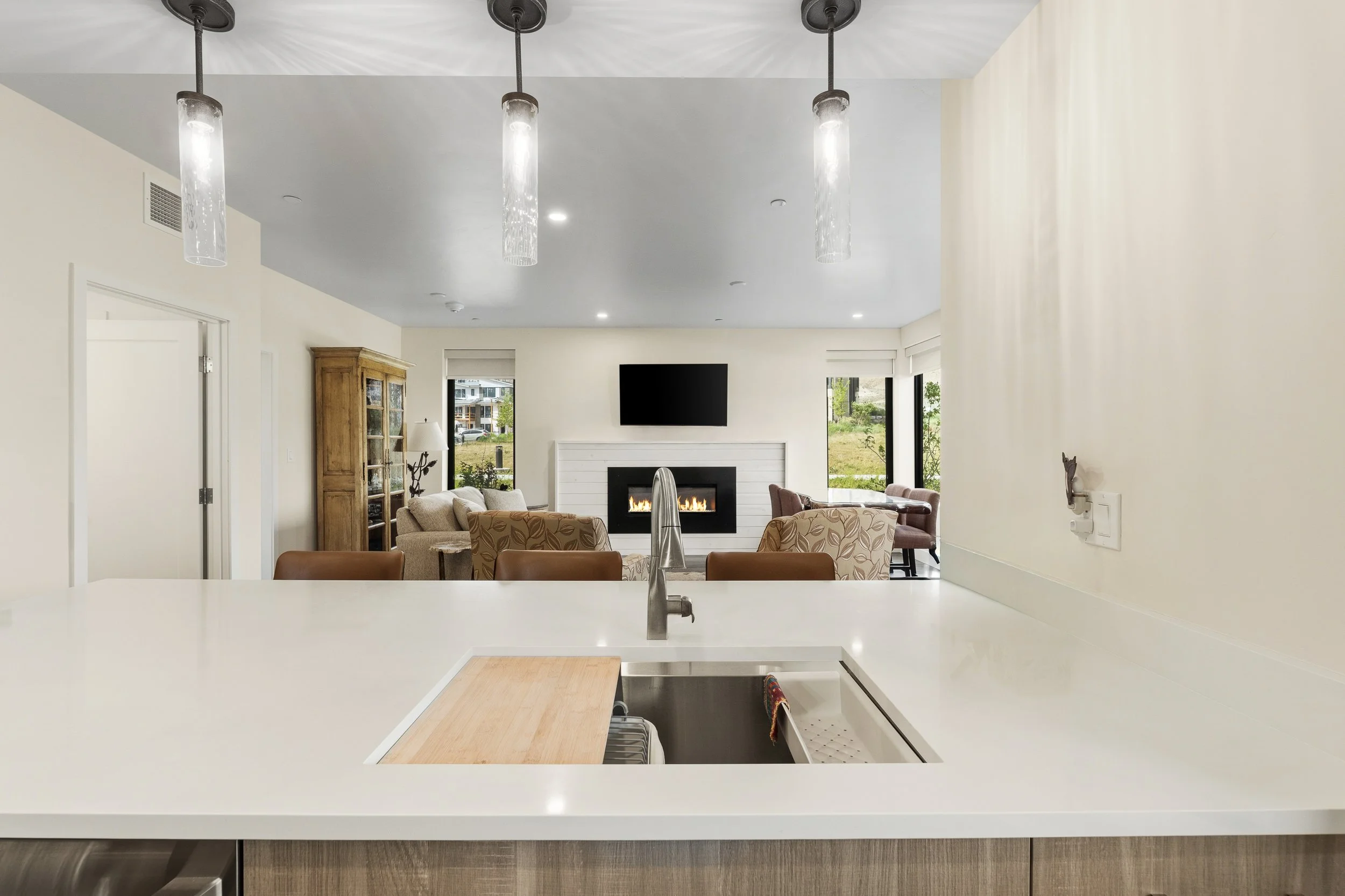 Modern kitchen with white countertops, visible sink, and a view into a living room with a fireplace, television, and seating area.