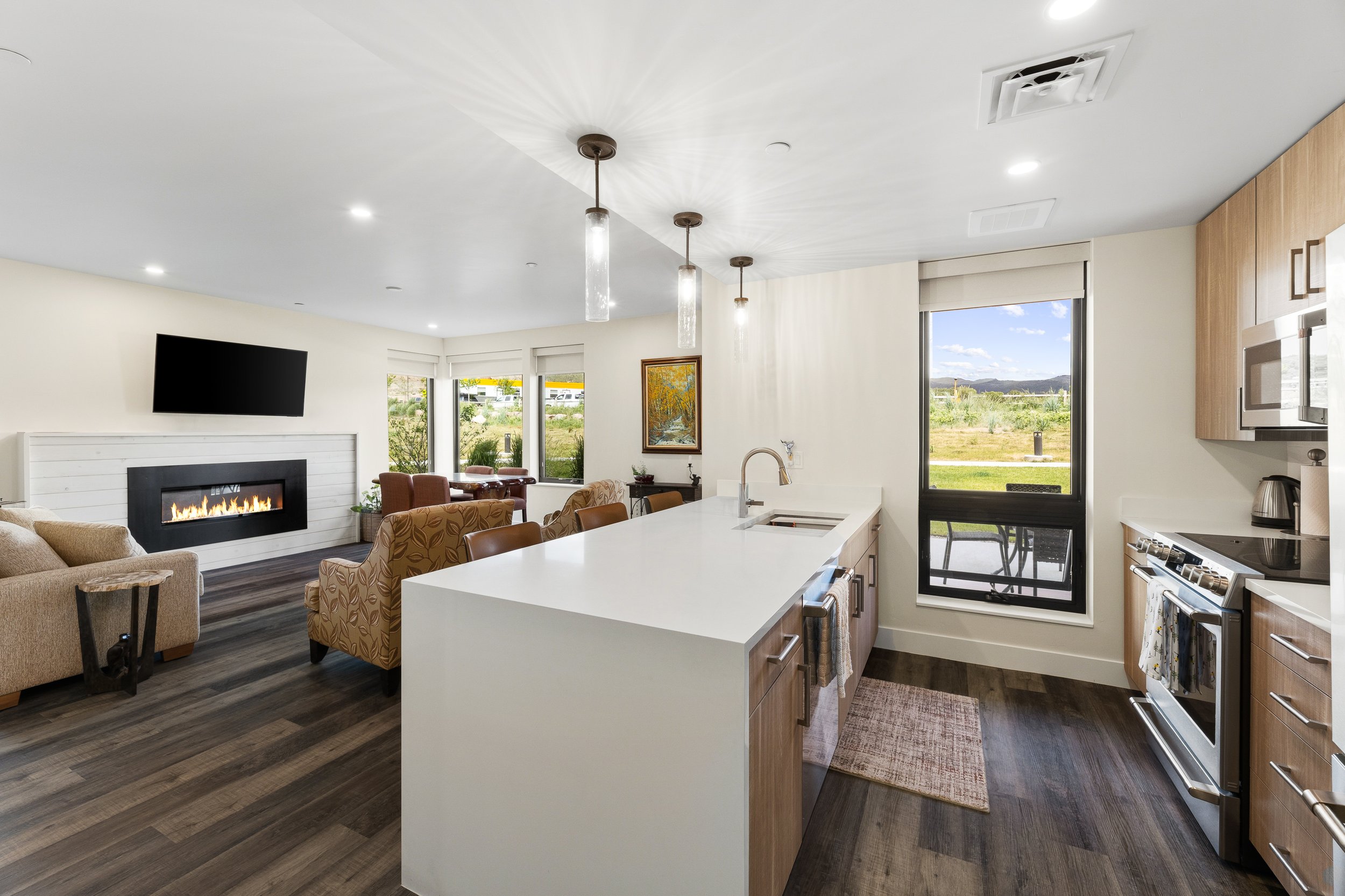 Open-concept living room and kitchen with large windows, modern decor, fireplace, and hardwood floors.
