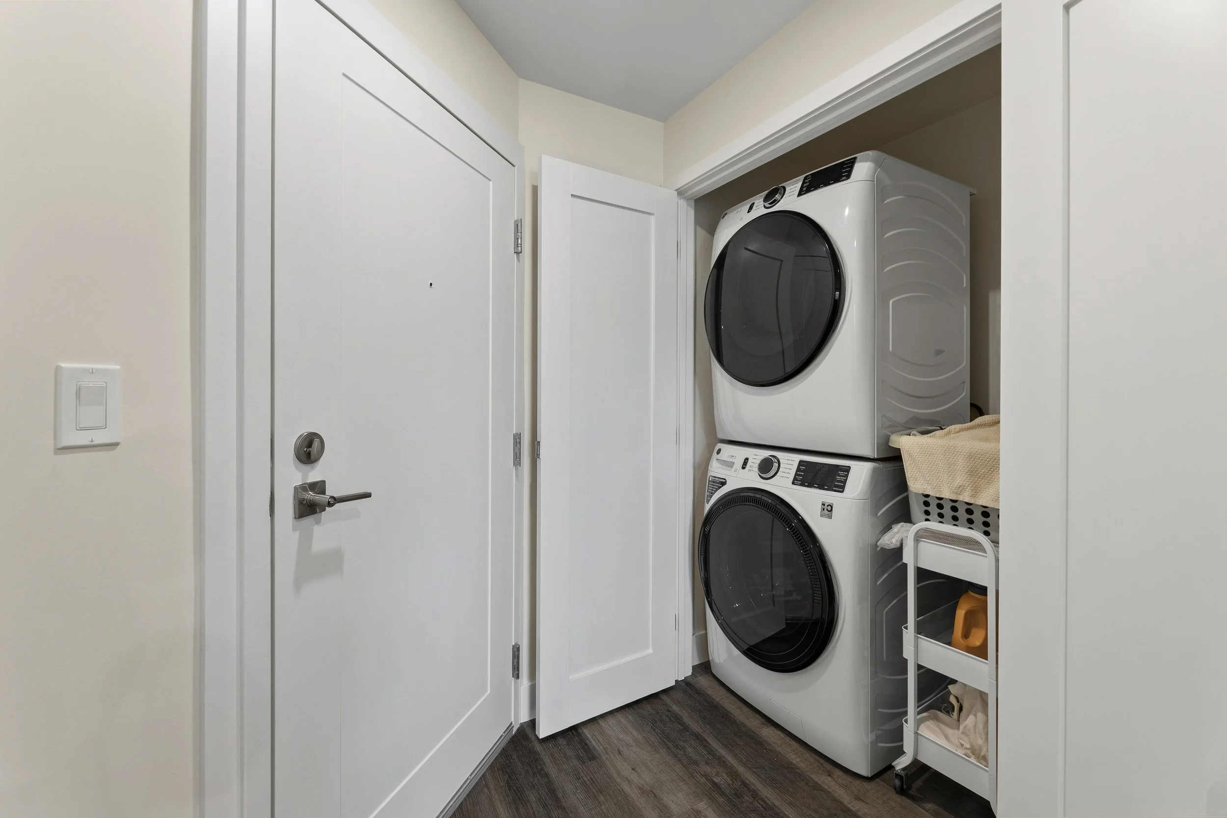 A laundry area with a front-loading washing machine and dryer stacked on top of each other in a small room with white walls and a white door.
