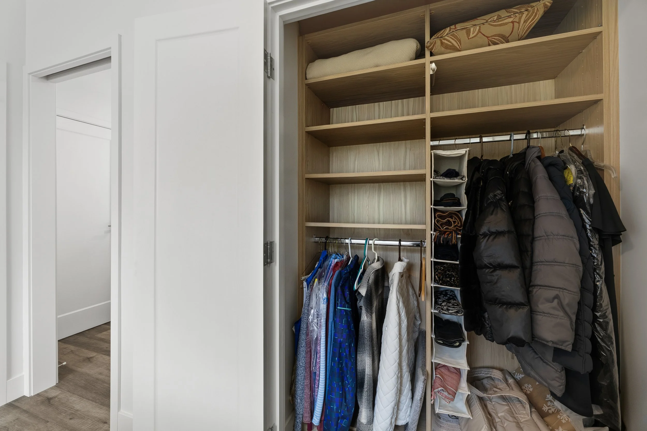 View of a closet with wooden shelving, hanging clothes, and folded linens.