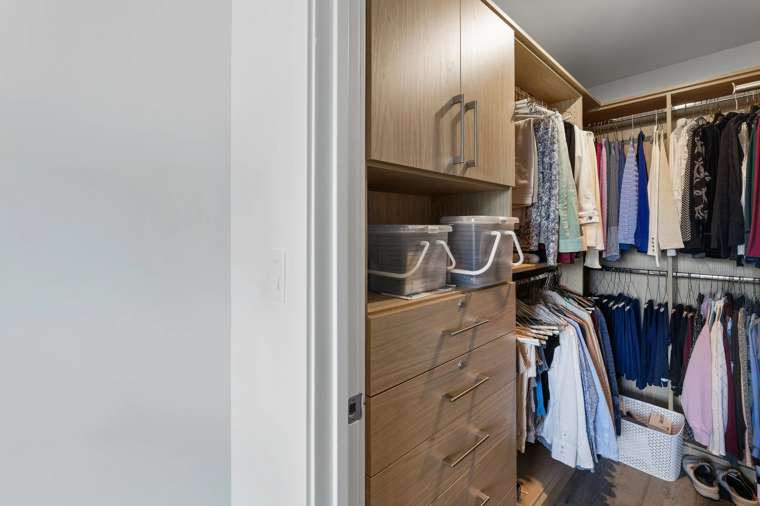 A walk-in closet with wooden drawers, shelves, and hanging space for clothes, shoes, and storage bins.