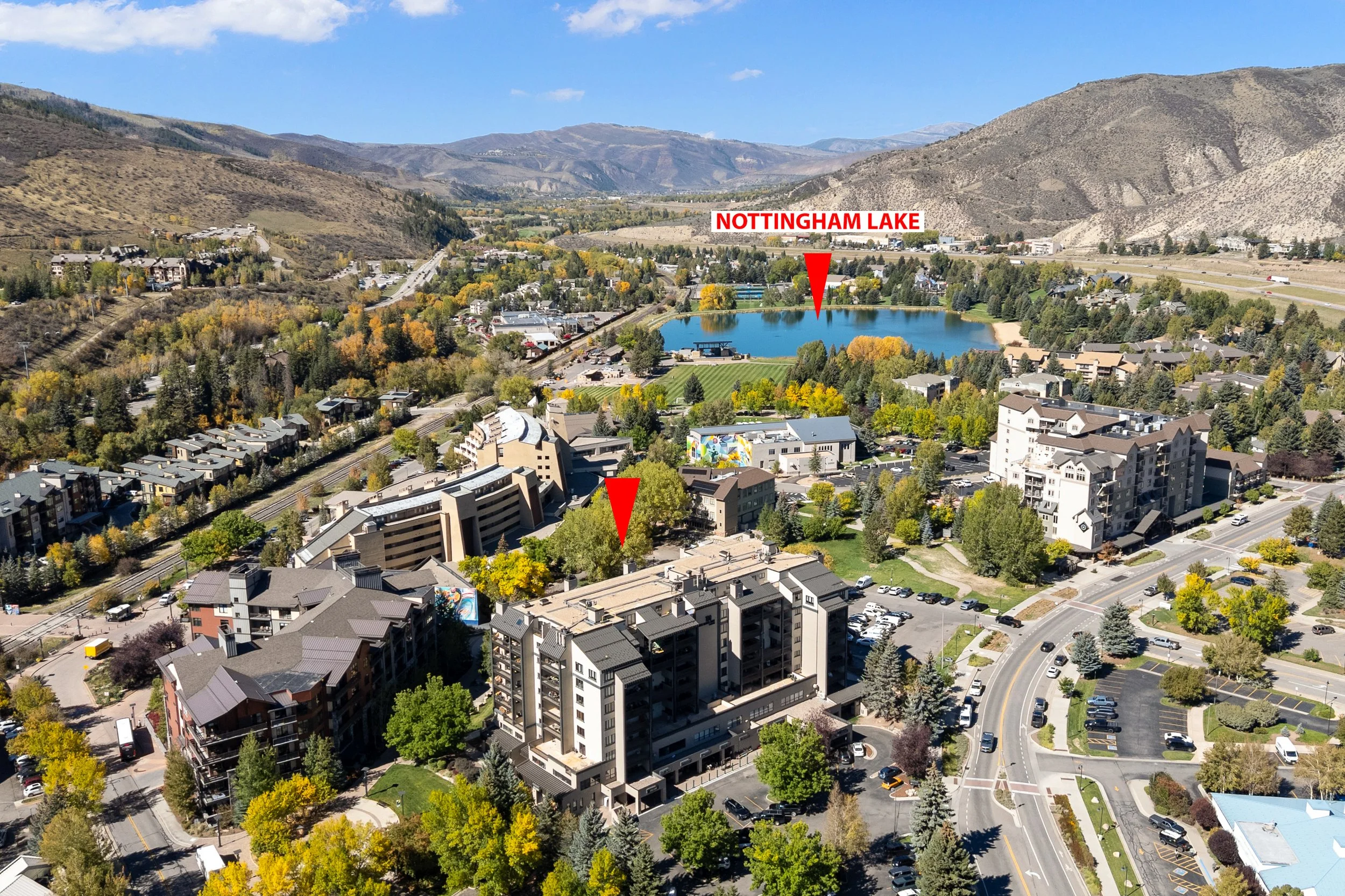 Aerial view of a town with a lake labeled Nottingham Lake surrounded by trees, buildings, and mountains under a clear blue sky.