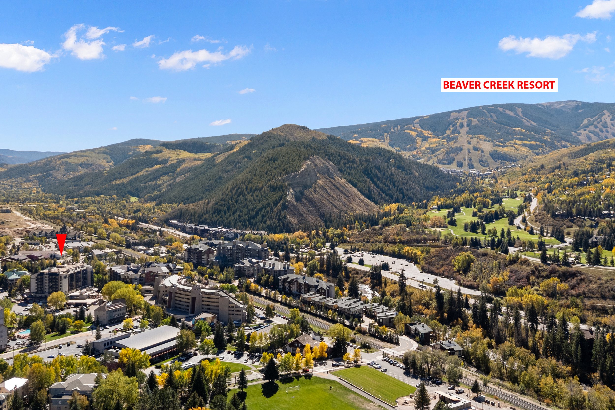Aerial view of a mountain landscape with green forests, ski slopes, and a small town with residential buildings and parking lots, labeled Beaver Creek Resort.