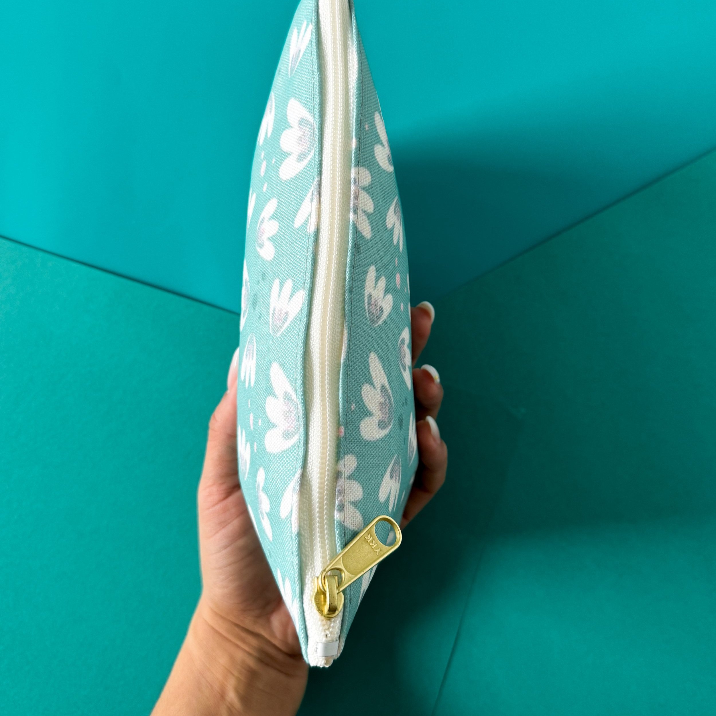 hand holding a small zipper pouch with flower pattern, cream, teal, light pink