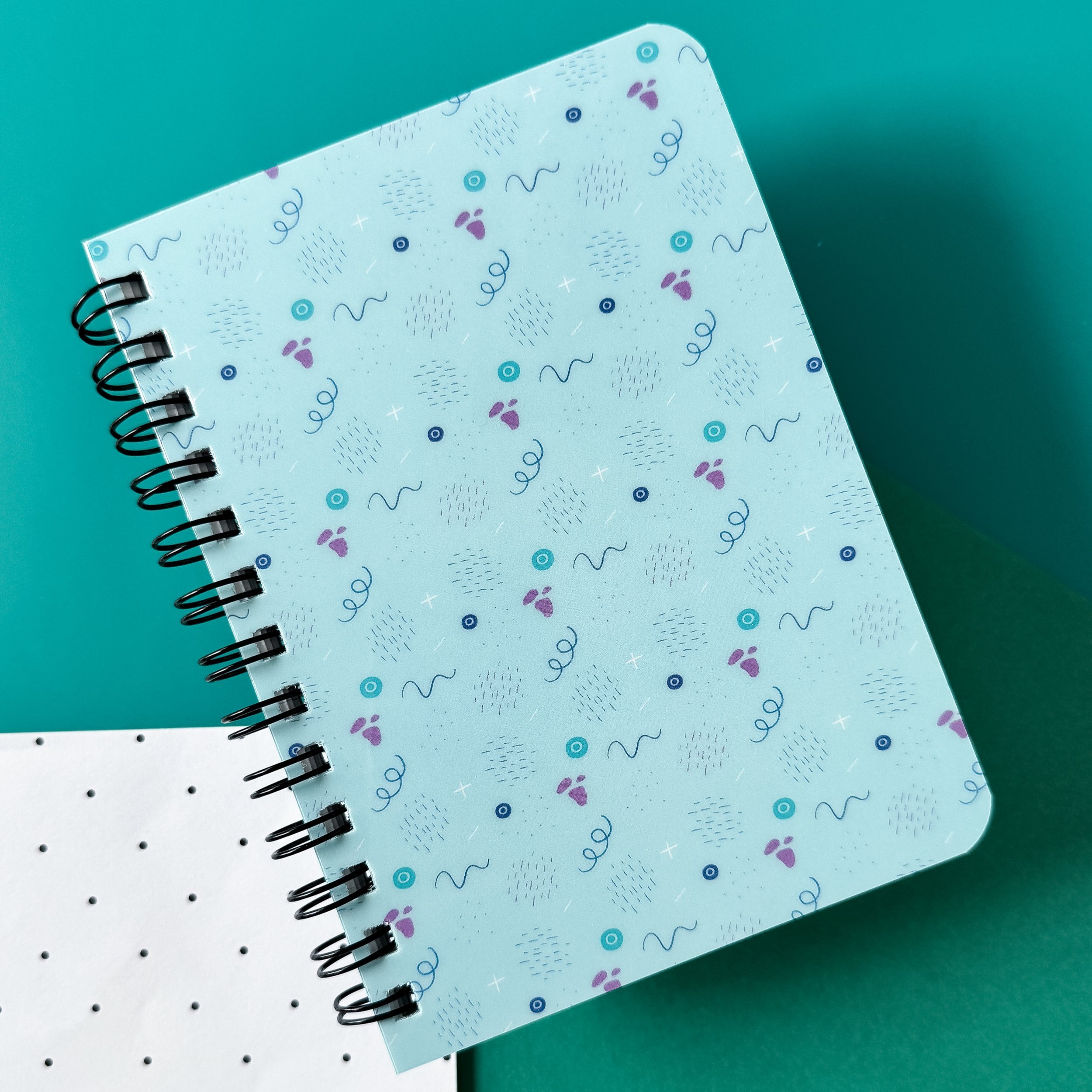 office supplies with spiral bound notebook with a pattern of lines and abstract shapes against a teal background