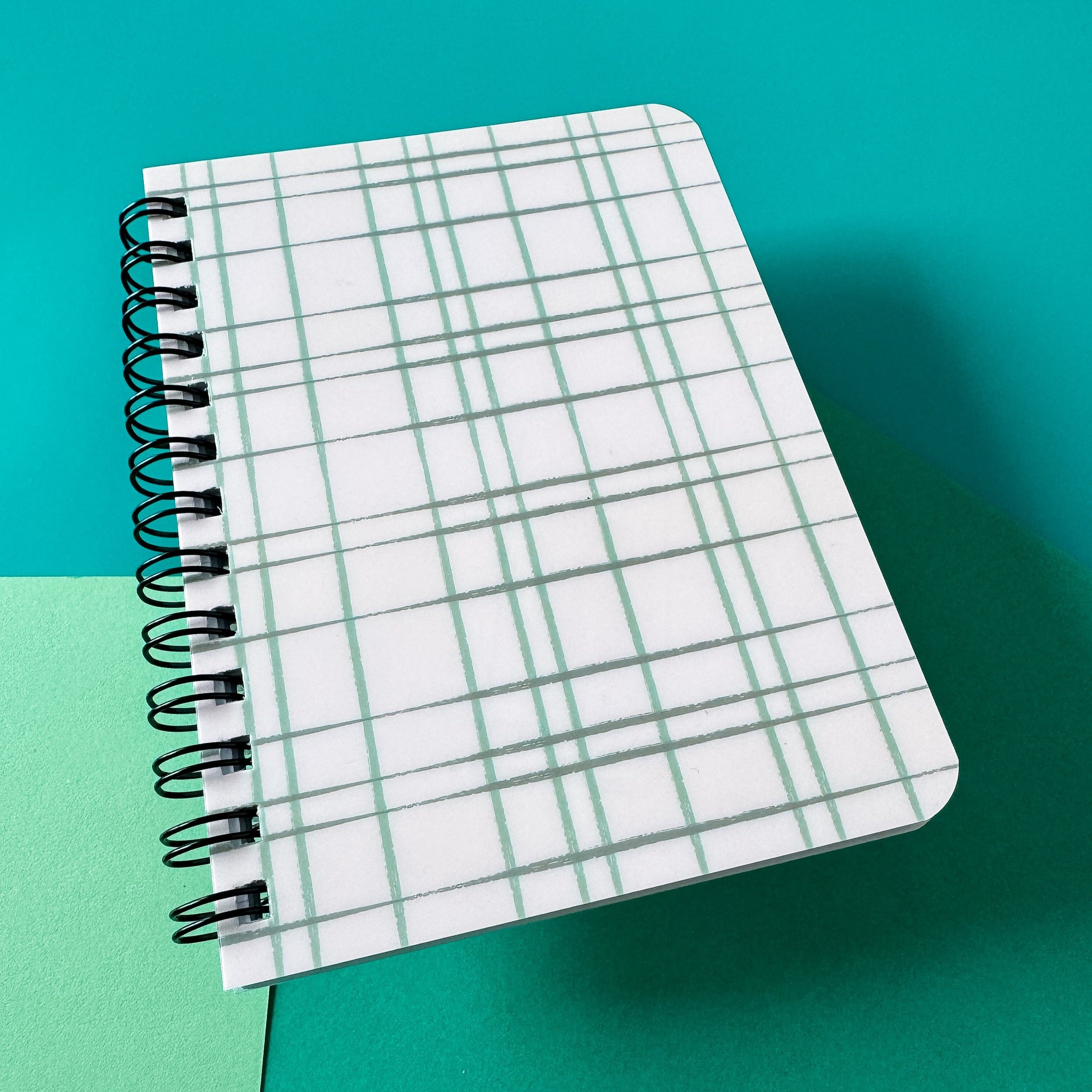 spiral bound notebook with lines pages and shiny cover with hand drawn line pattern on top on teal background