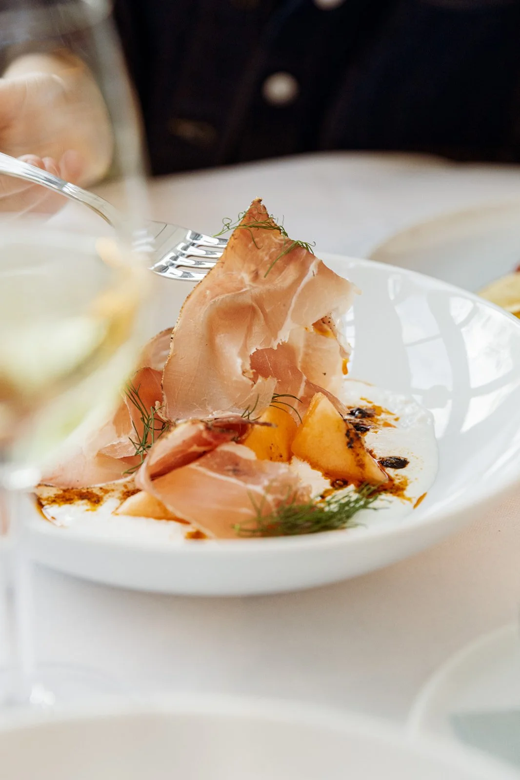 A delicate dish featuring slices of ham, roasted peaches, and fresh herbs on a white plate.