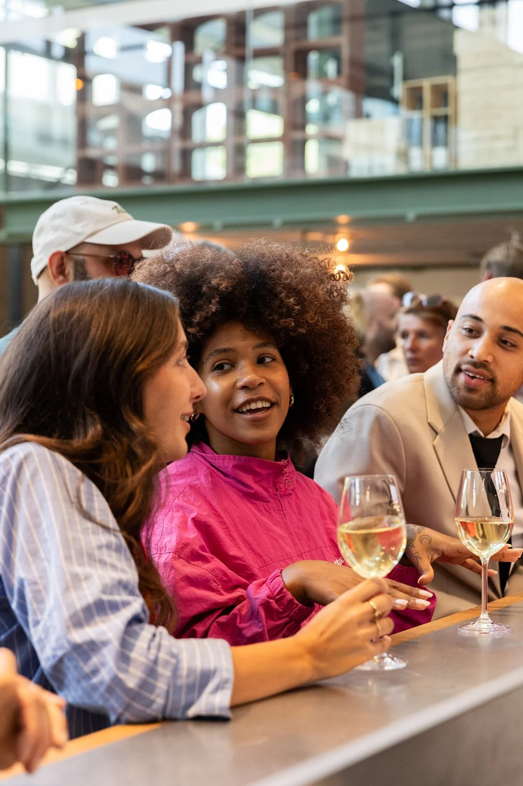 Five people sitting at a bar or table, enjoying white wine, in a cozy, bustling atmosphere.
