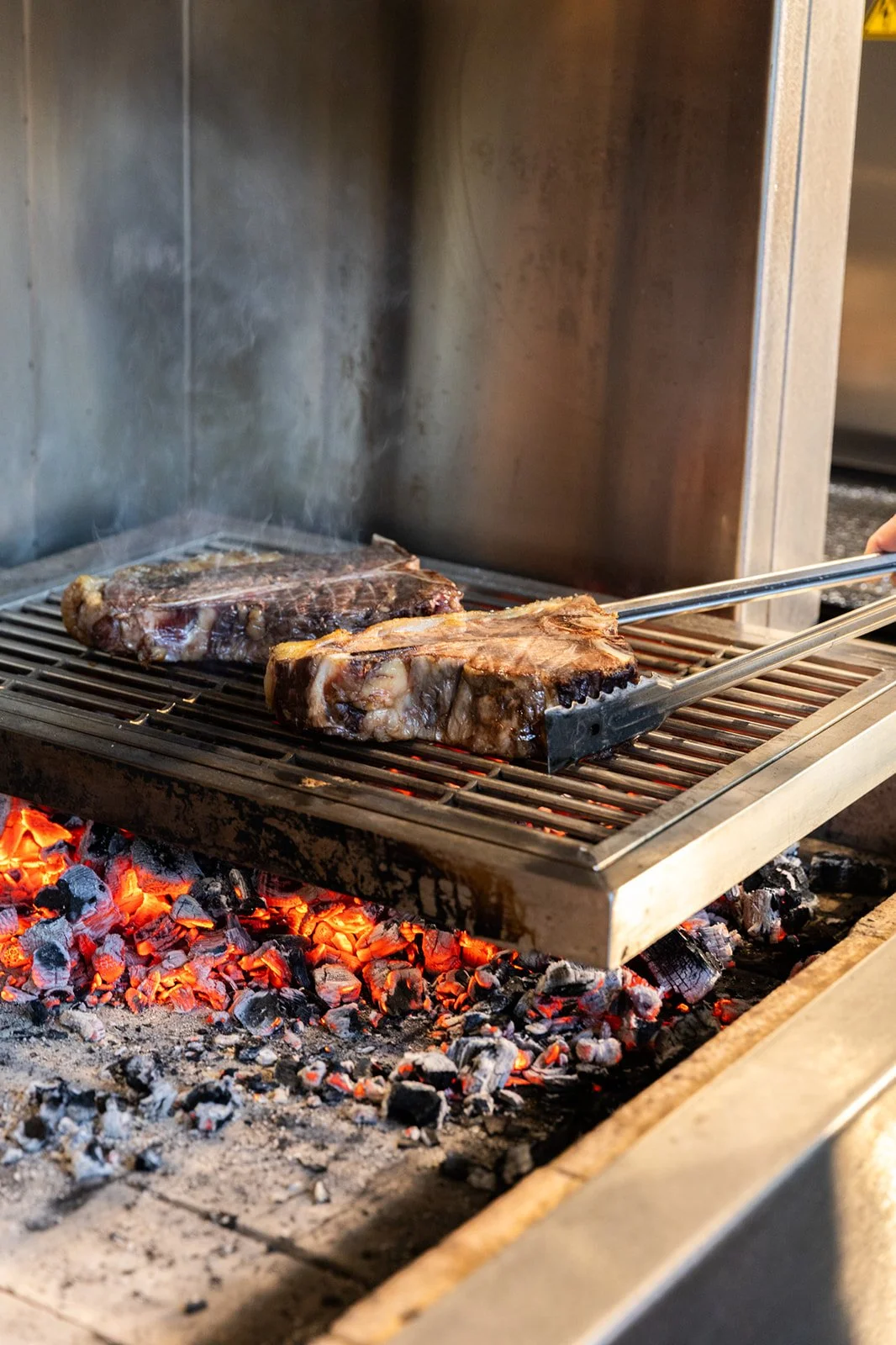 Two large cuts of meat being cooked on a barbecue grill over glowing charcoal.