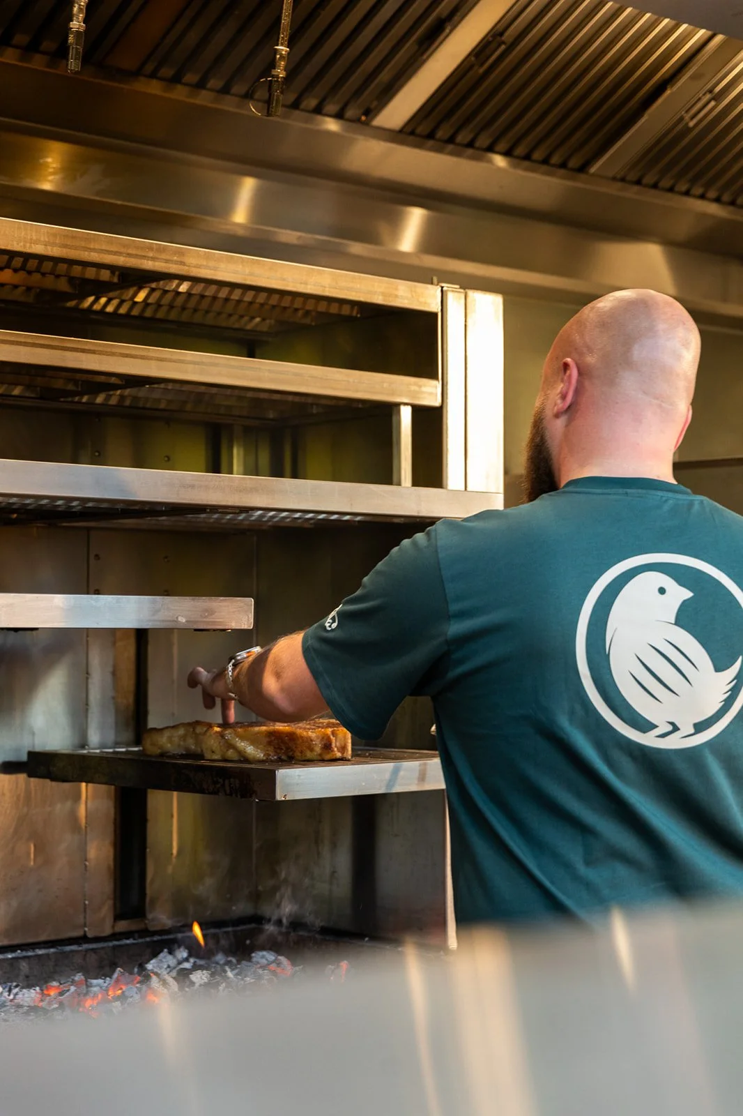 A man is cooking meat on a grill in a professional kitchen.