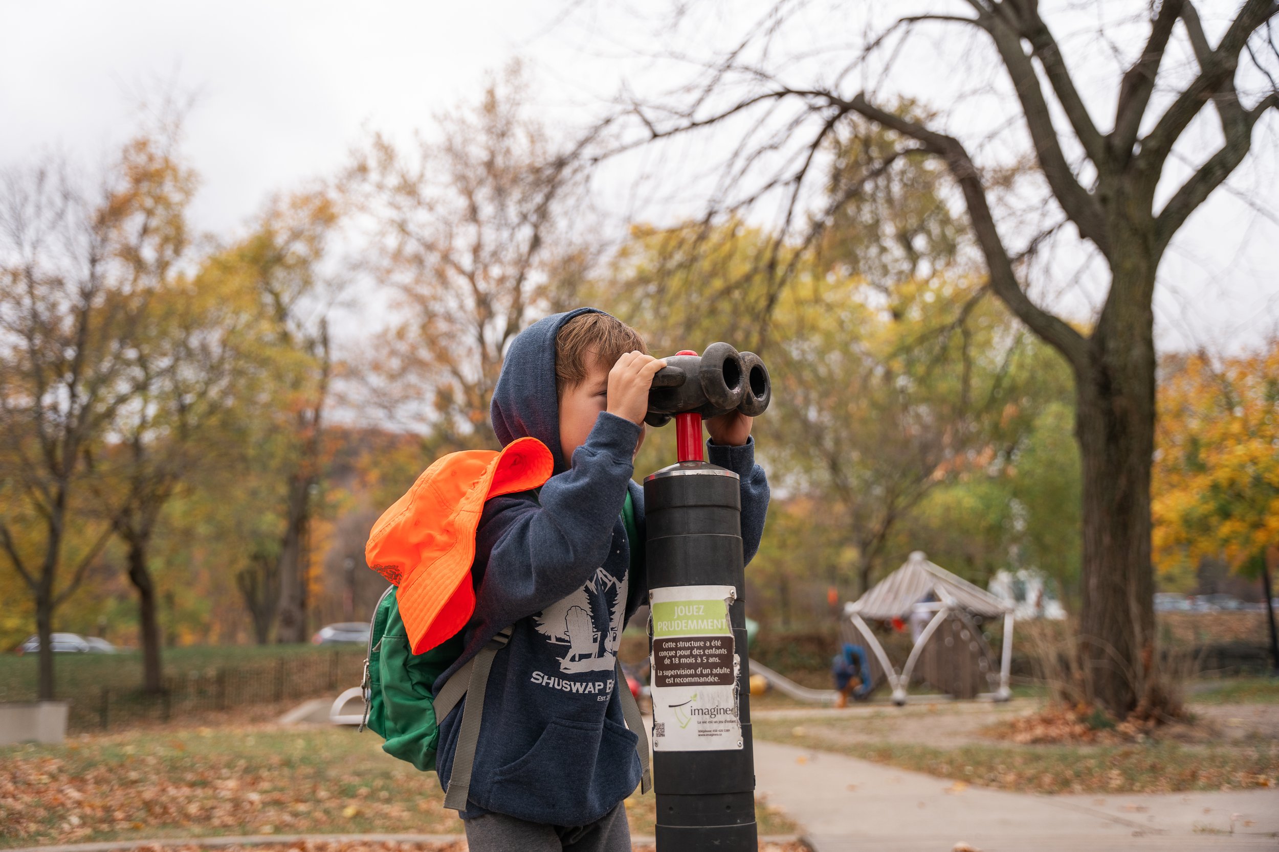 Child looking through playground telescope in autumn park